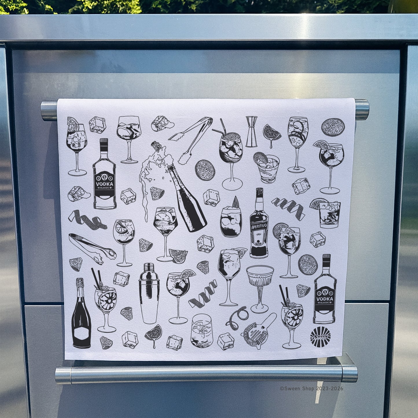100% cotton Tea towel with black aperol spritz cocktail illustrations hanging on a stainless steel oven door.