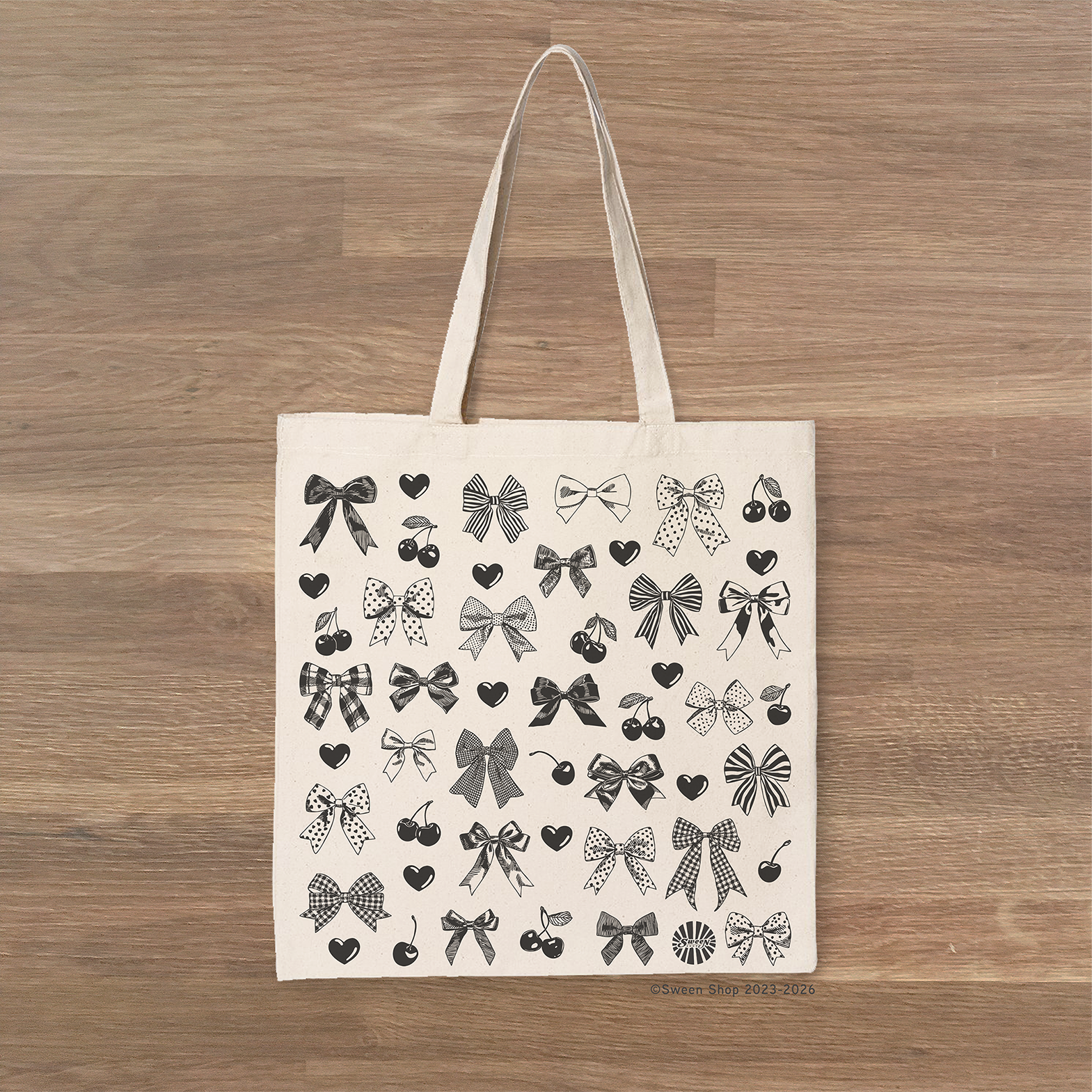 Tote bag with black bow heart and cherry pattern on a wooden surface