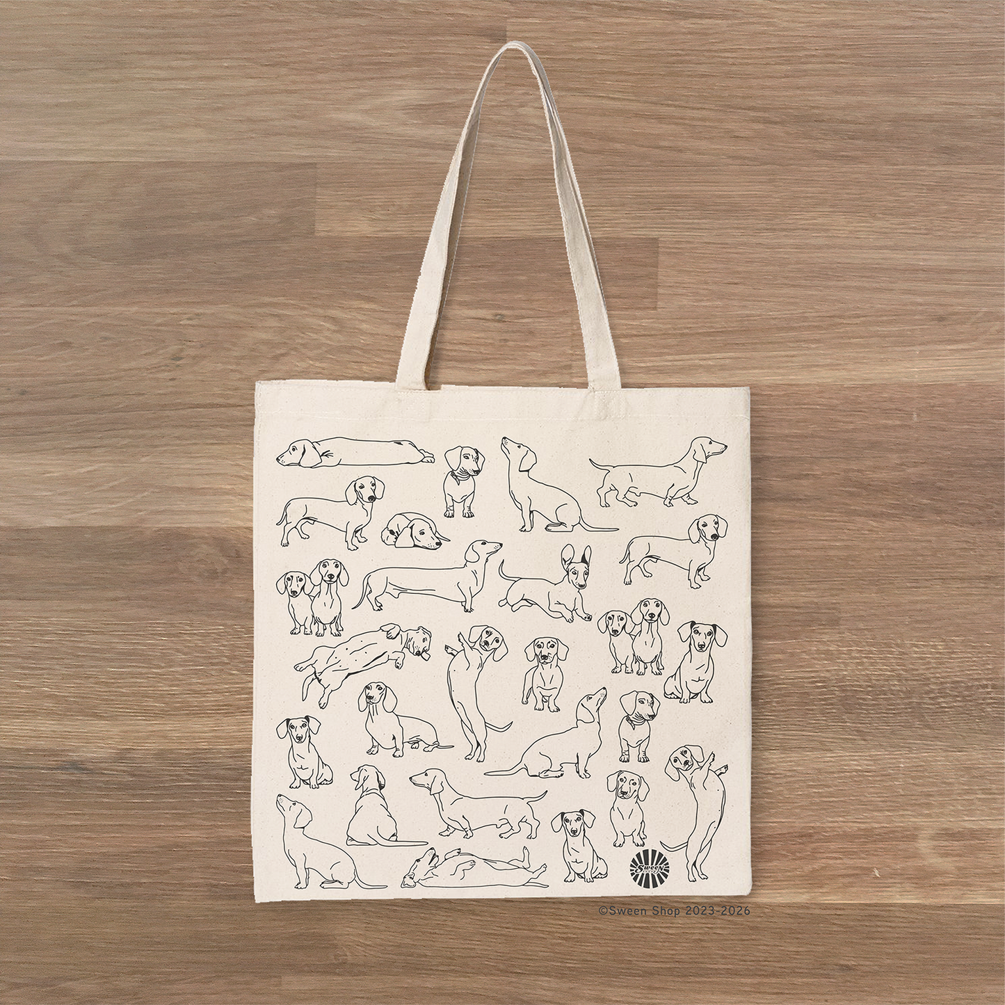 cotton canvas Tote bag with black line drawings of dachshund pet dogs on a wooden surface