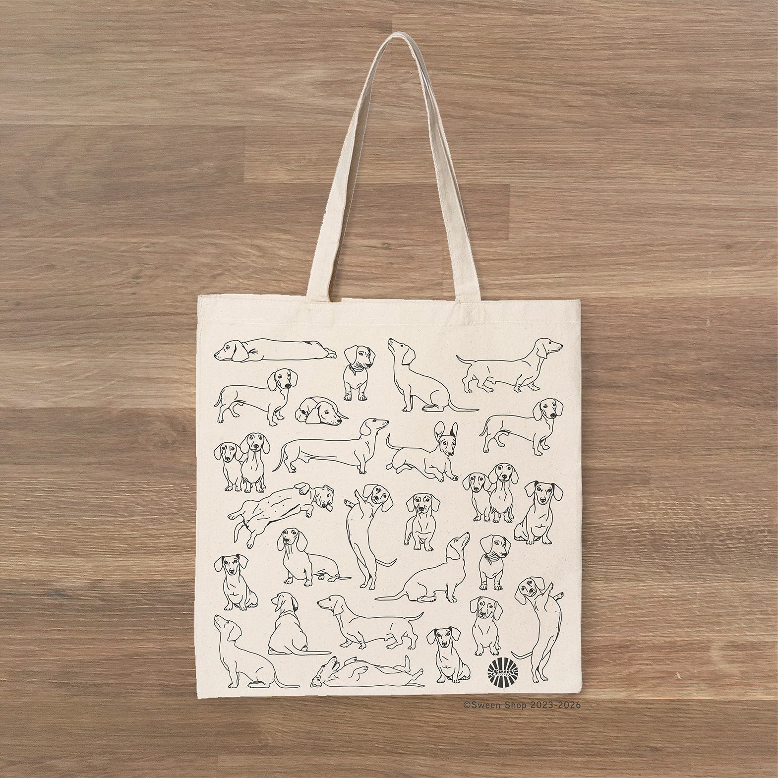 cotton canvas Tote bag with black line drawings of dachshund pet dogs on a wooden surface