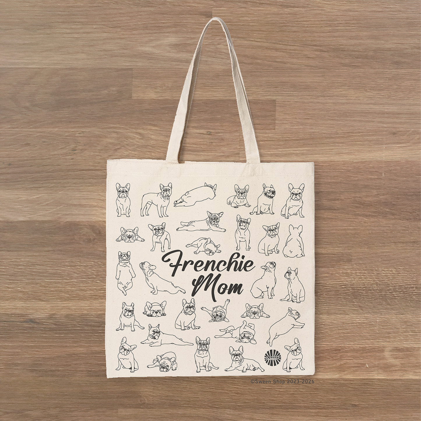 Tote bag with 'Frenchie Mom' text and french bulldog pet dog illustrations on a wooden surface