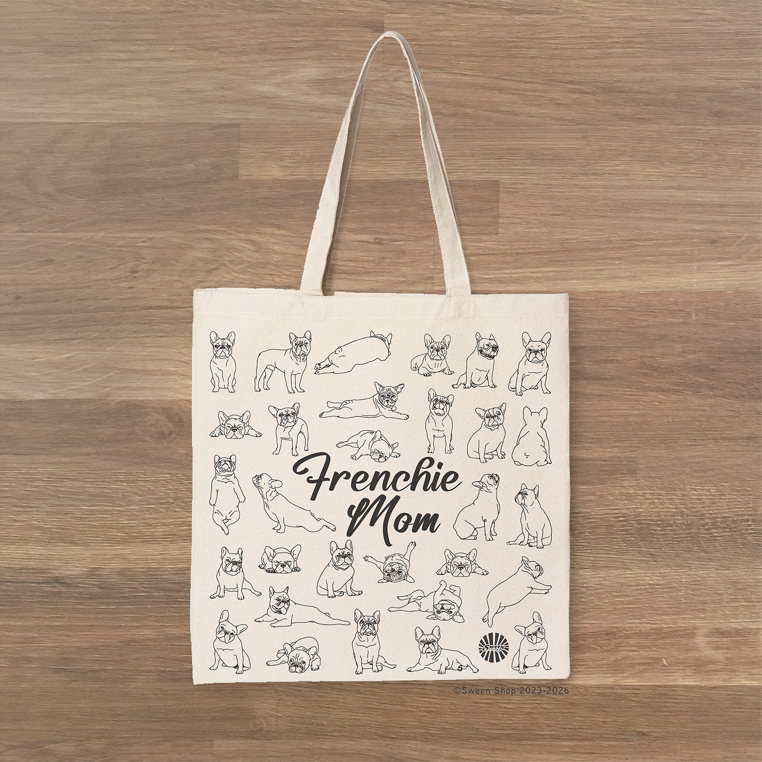 Tote bag with 'Frenchie Mom' text and french bulldog pet dog illustrations on a wooden surface