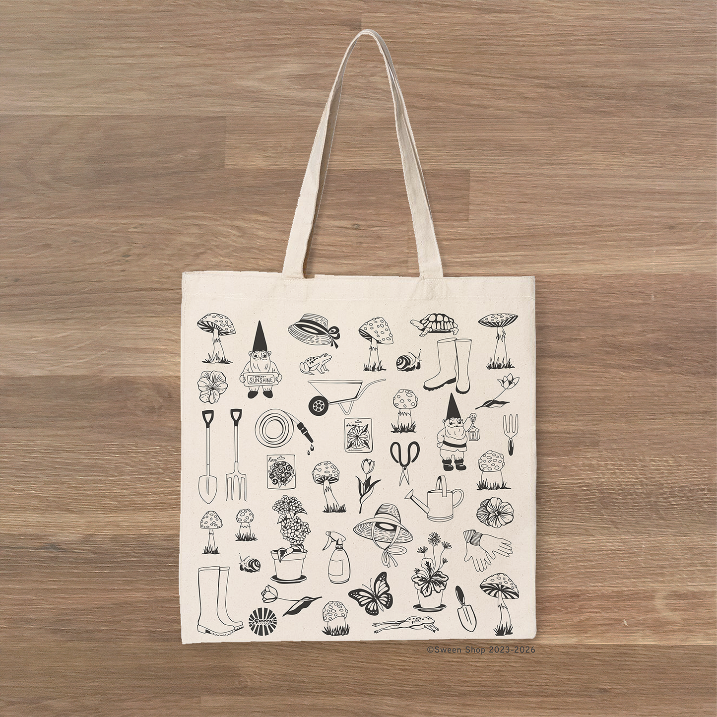 Tote bag with black garden themed illustrations on a wooden surface