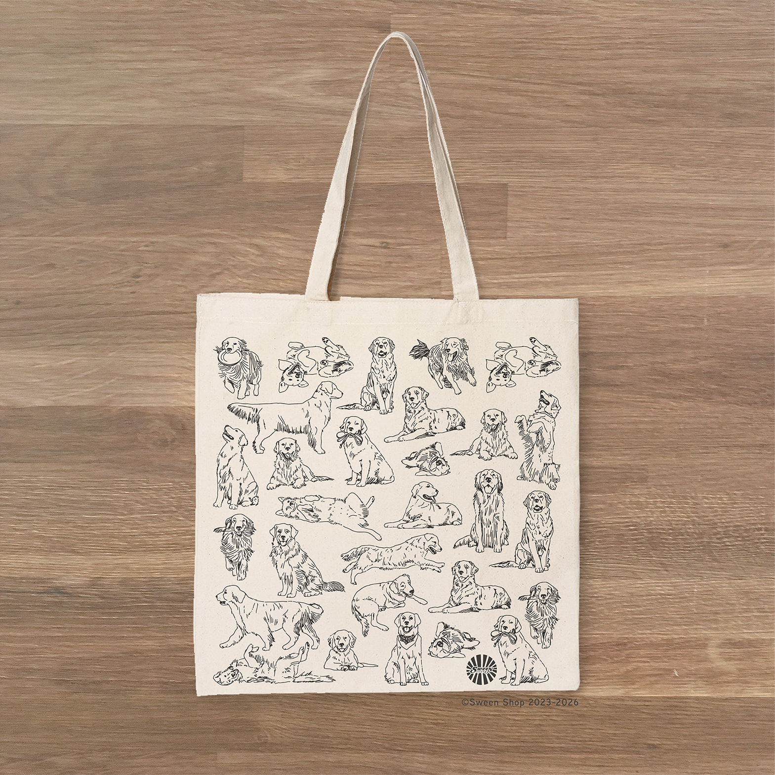 Tote bag with black line drawings of golden retriever pet dogs on a wooden surface