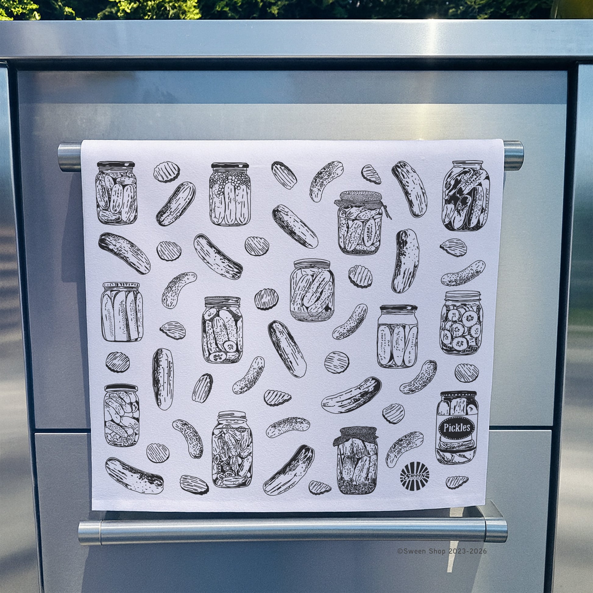 Towel with pickle and jar pattern hanging on a stainless steel oven