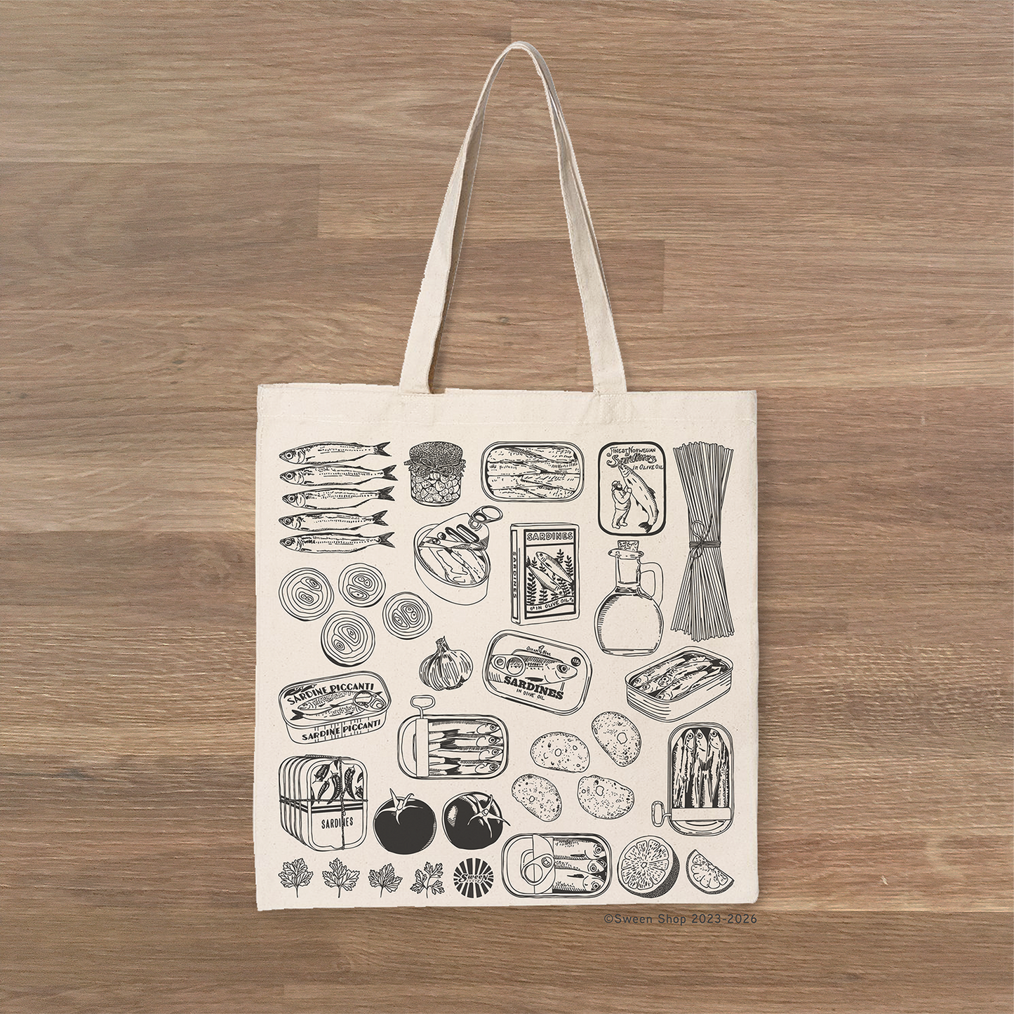 Tote bag with black sardine canned fish pasta tomato illustrations on a wooden surface