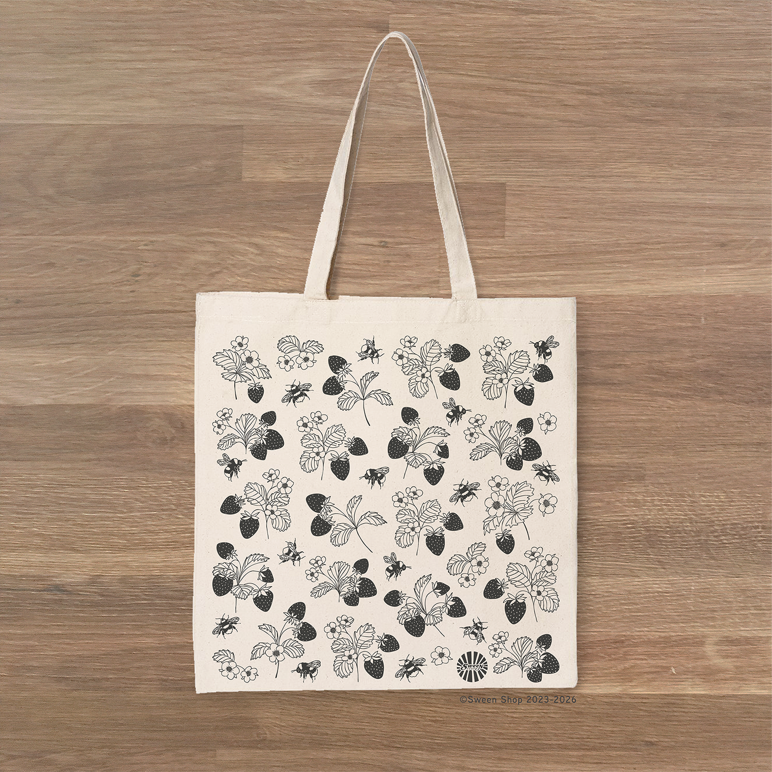 Tote bag with black floral strawberry bumble bee pattern on a wooden surface