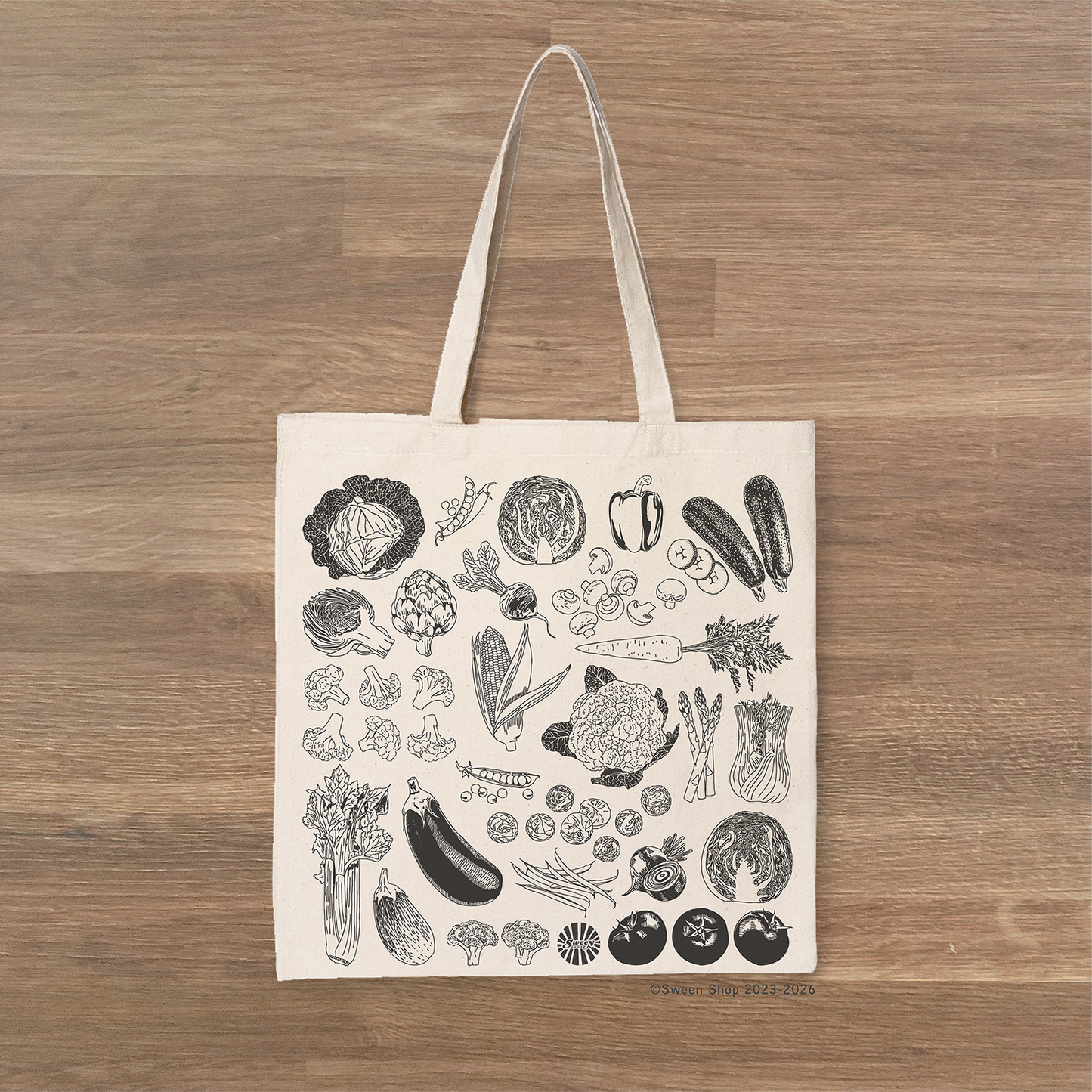 Tote bag with black vegetable illustrations on a wooden surface