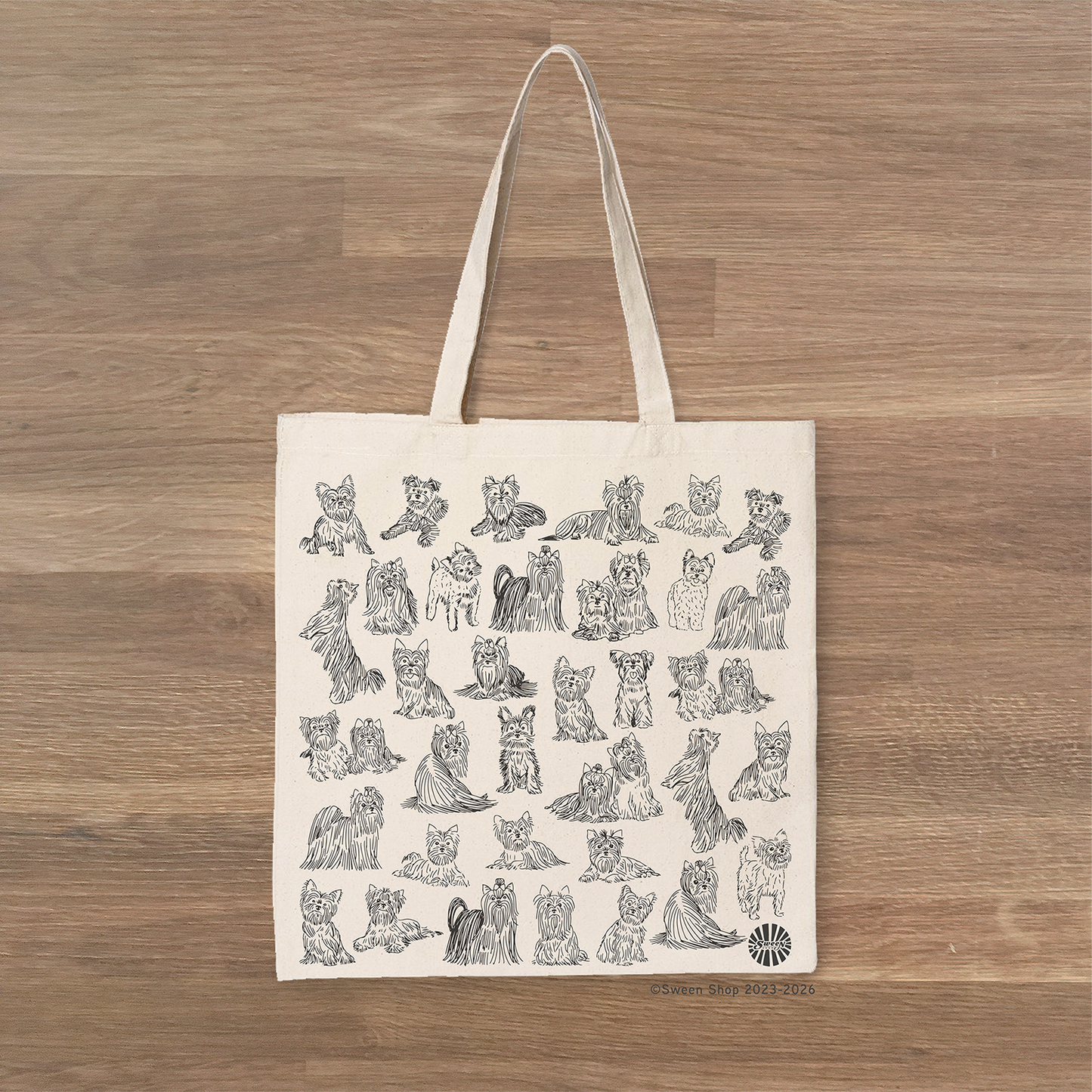 Natural cotton canvas Tote bag with black drawings of yorkshire terrier dogs on a wooden surface