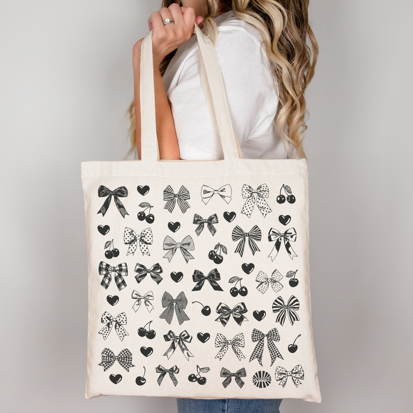Tote bag with black bow heart and cherry hand drawn printed pattern held by a person against a plain background
