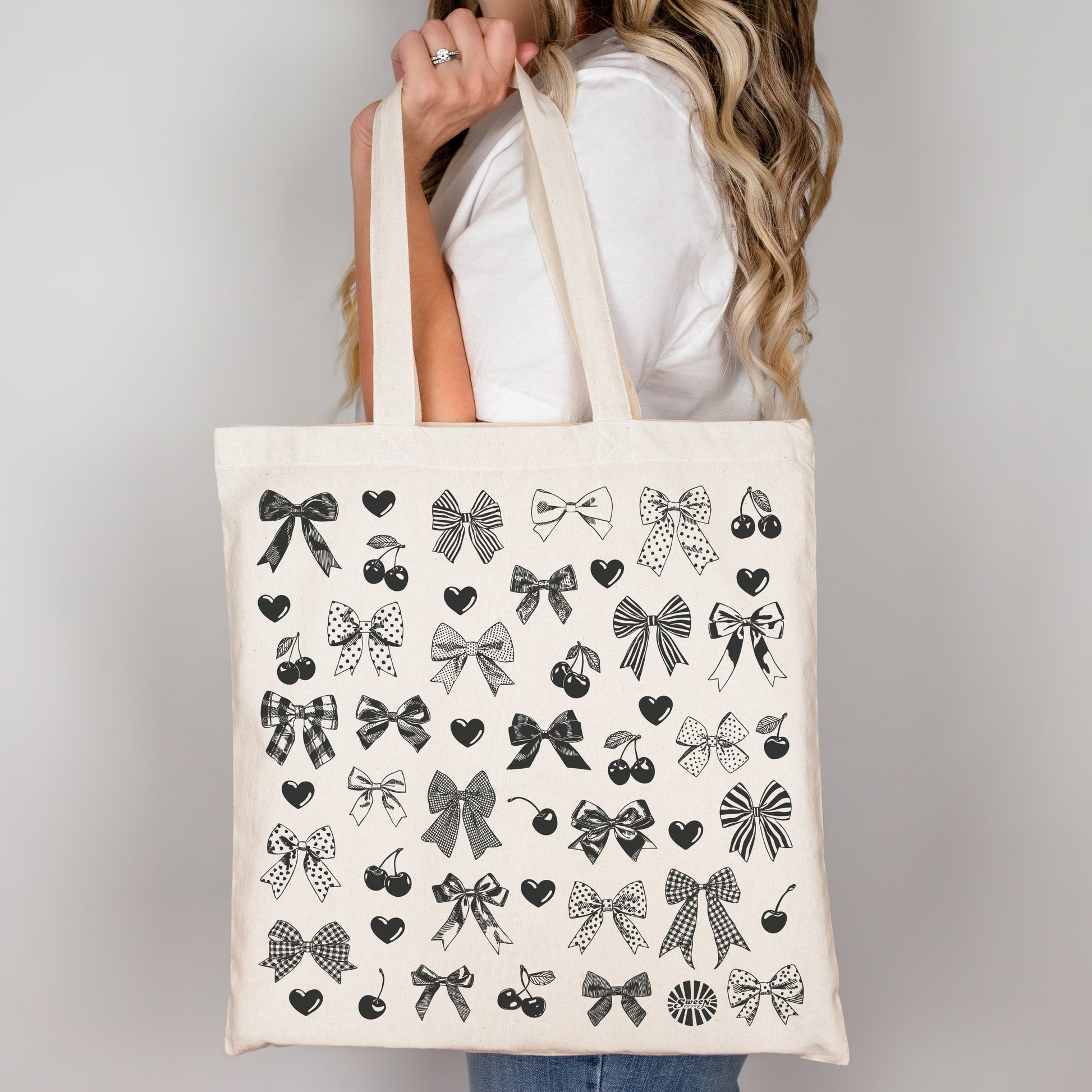 Tote bag with black bow heart and cherry hand drawn printed pattern held by a person against a plain background