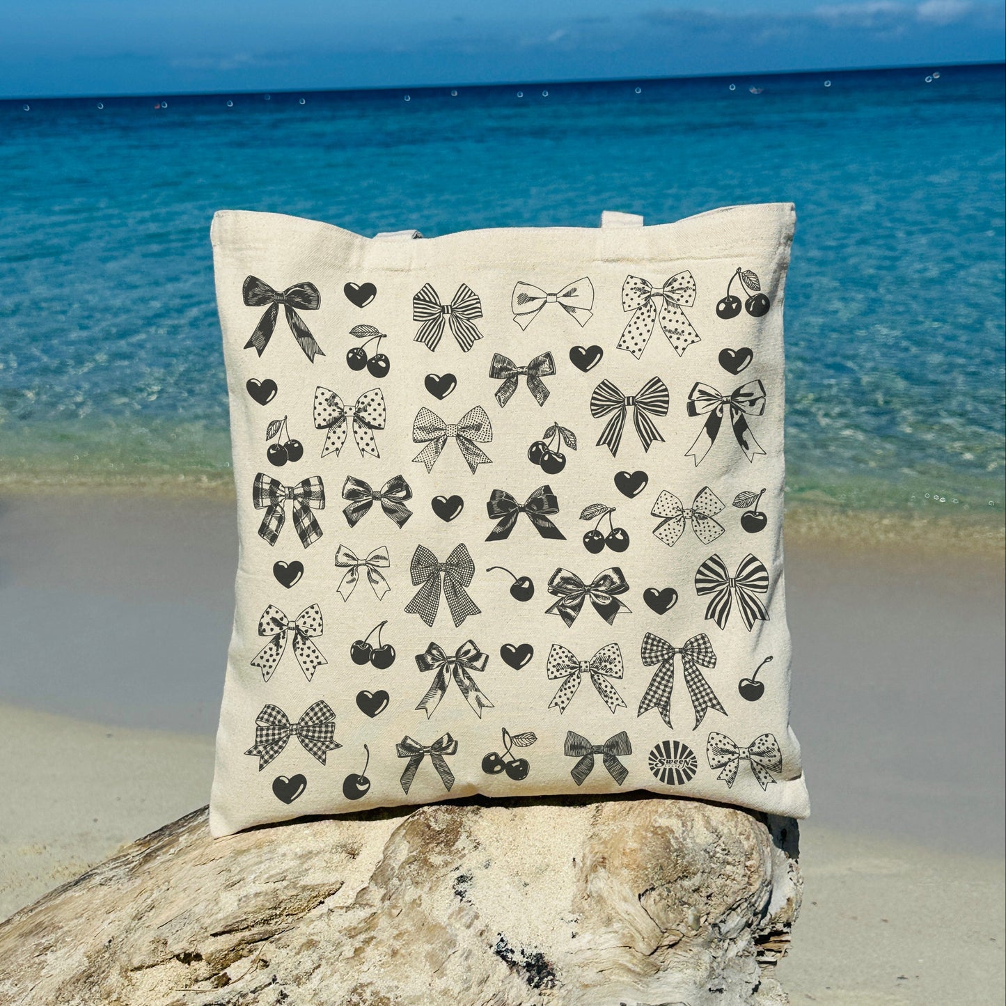 Natural cotton canvas tote bag with black bow cherry heart hand drawn print on a rock by the ocean