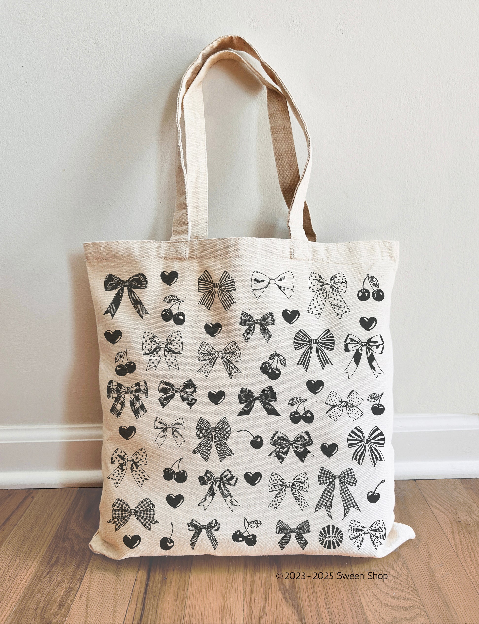Tote bag with black bow pattern on a wooden floor against a white wall
