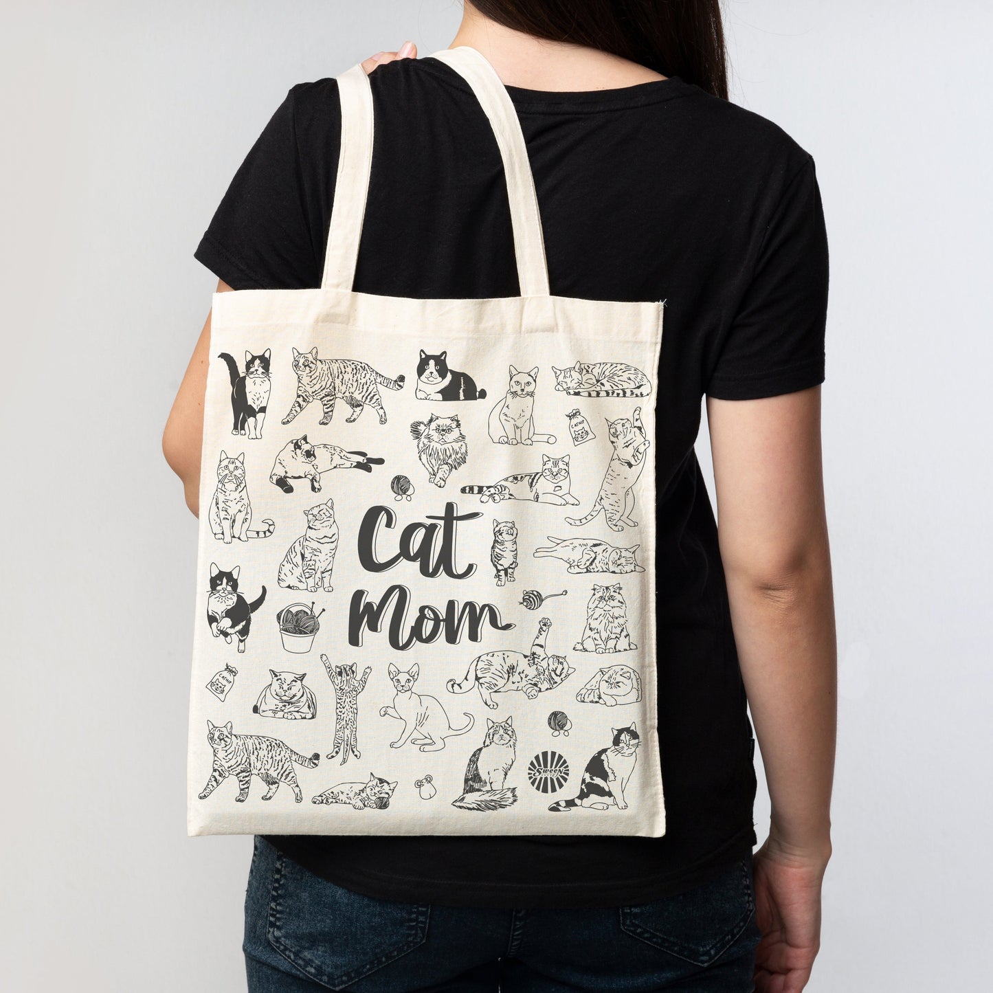 Person holding a tote bag with cat illustrations and 'Cat Mom' text against a plain background