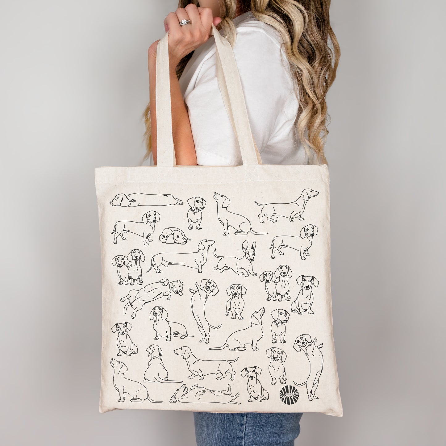 Tote bag with black line drawings of dachshund pet dogs held by a person against a plain background