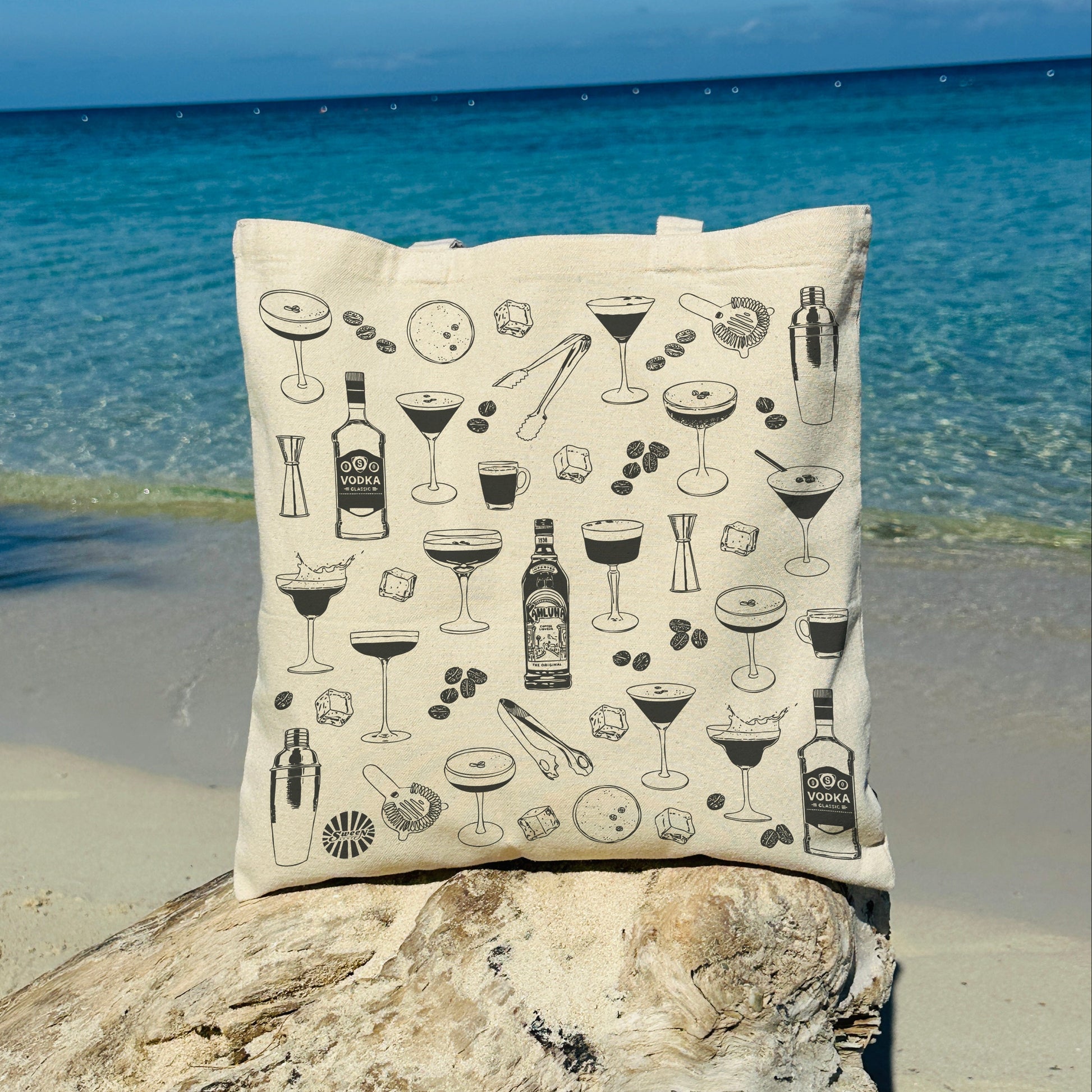 cotton canvas tote bag with espresso martini cocktail-themed design on a rock by the ocean