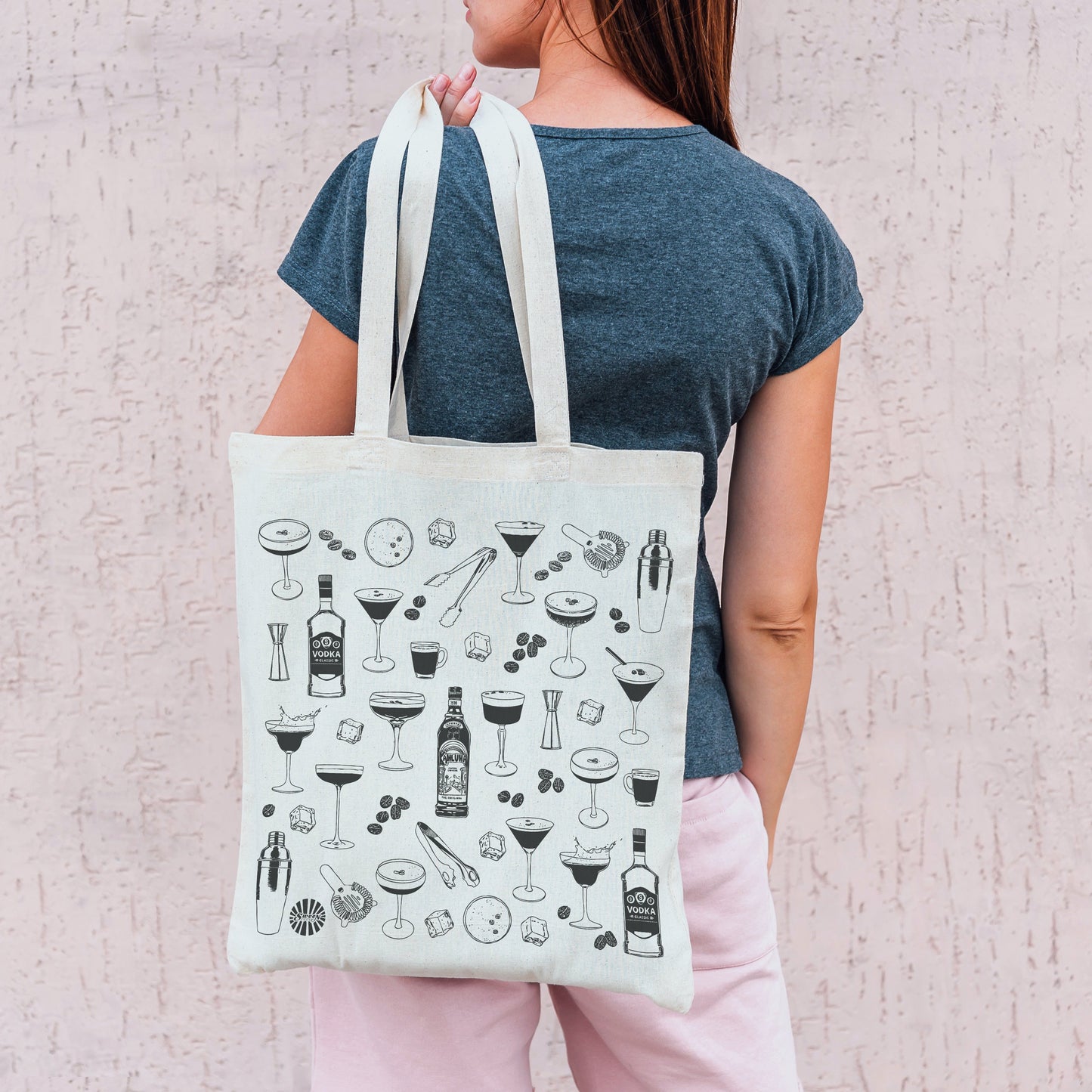 Person holding a tote bag with espresso martini drink icons against a light background