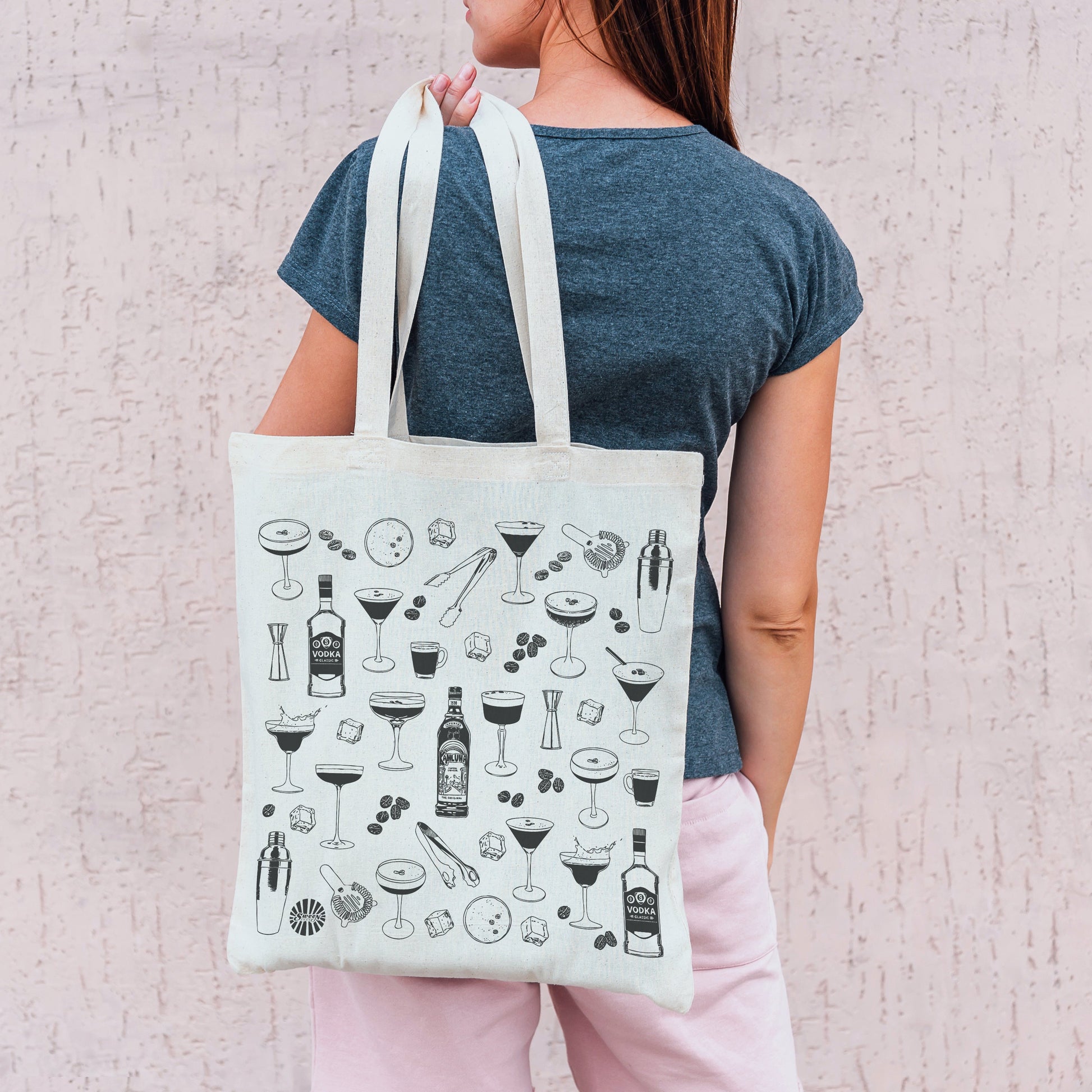 Person holding a tote bag with espresso martini drink icons against a light background