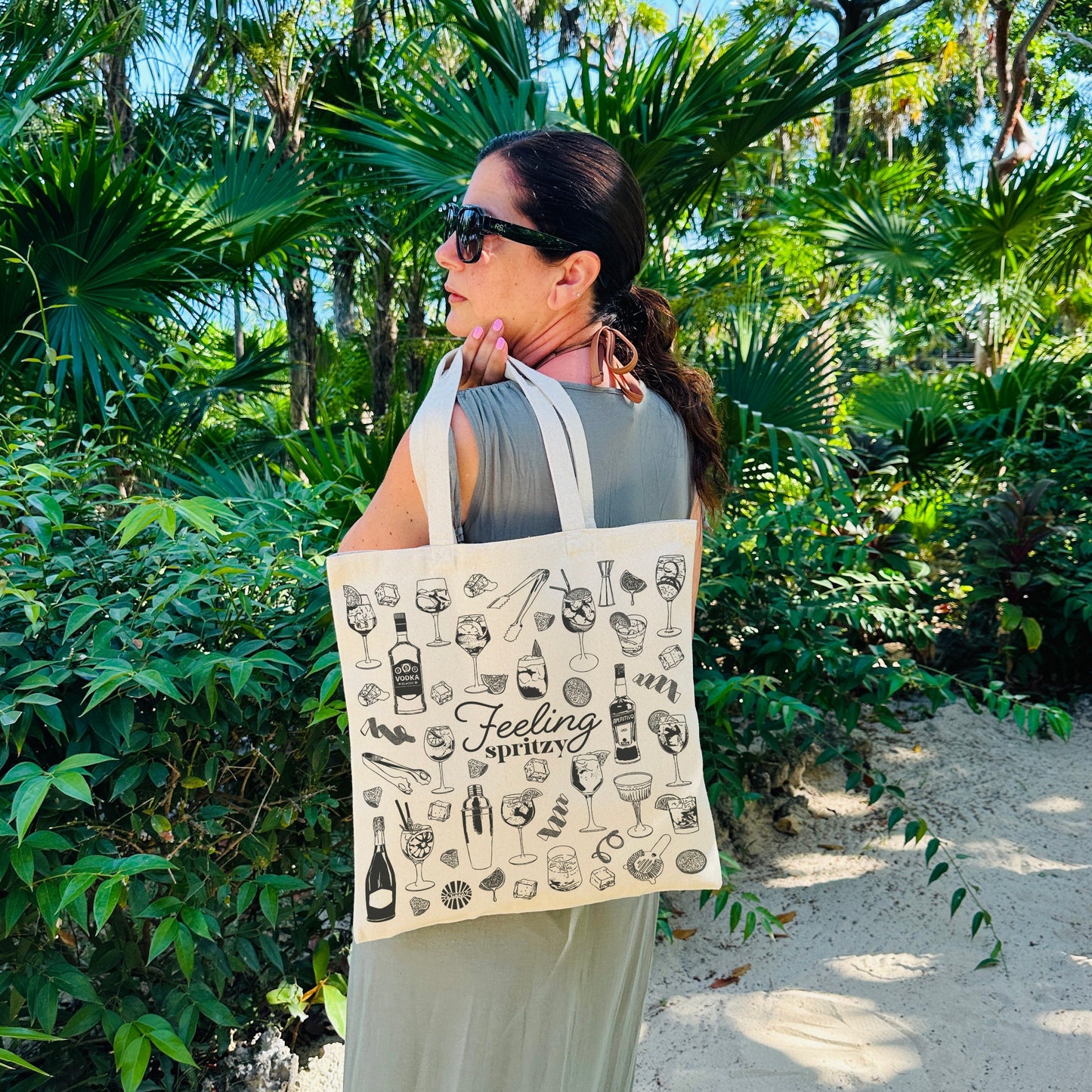 Woman holding a beach tote bag with a aperol spritz cocktail design in a tropical setting
