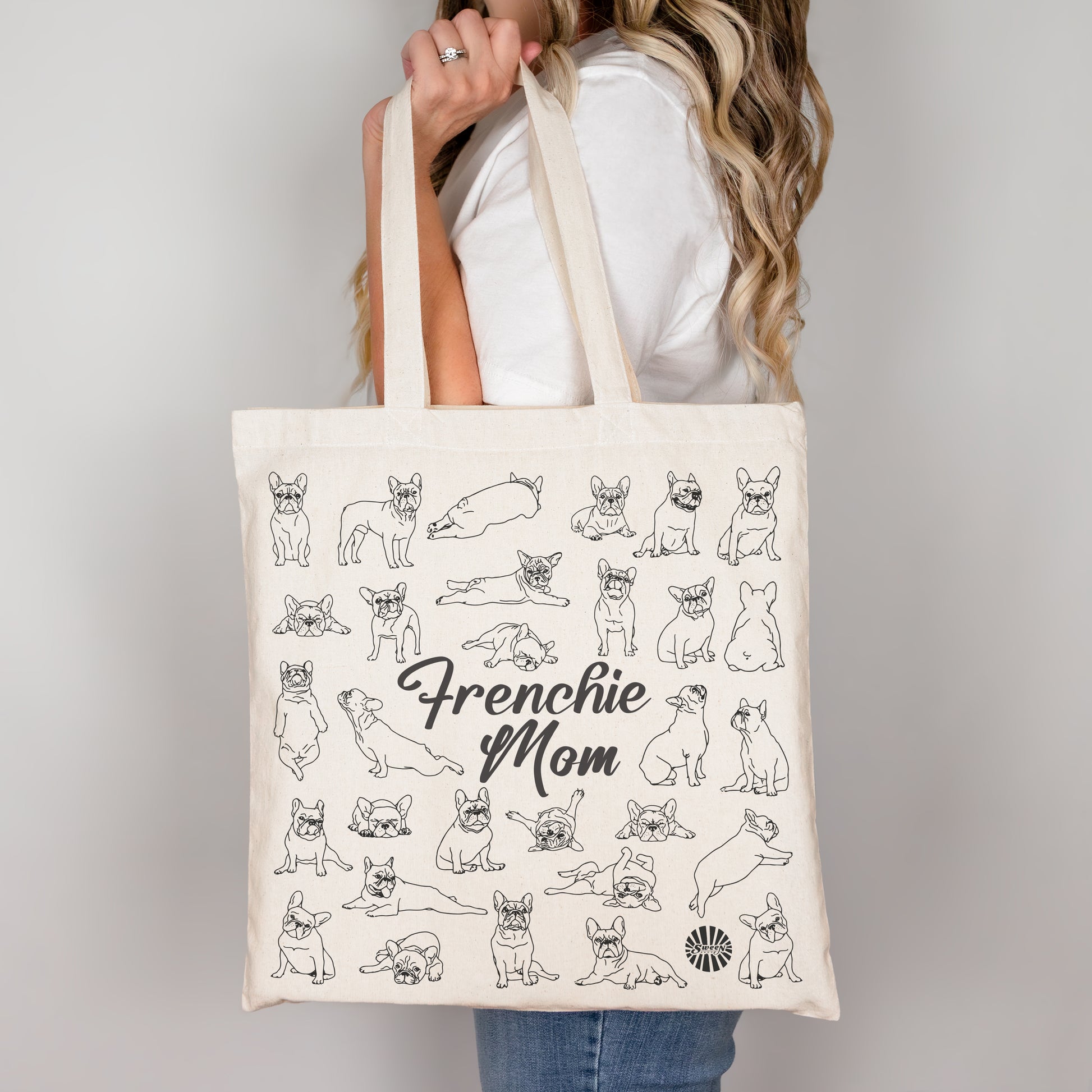 Tote bag with 'Frenchie Mom' text and french bulldog dog illustrations held by a person.