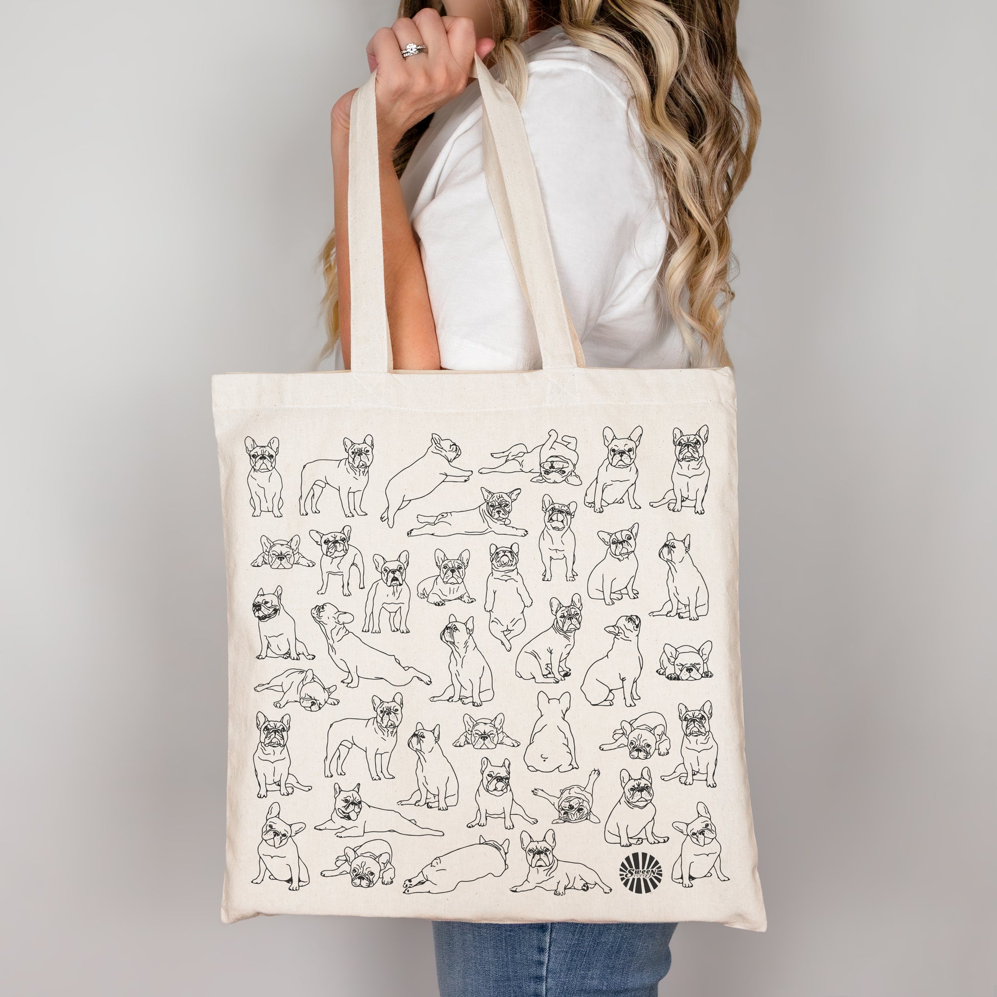Tote bag with black line drawings of french bulldogs held by a person against a plain background