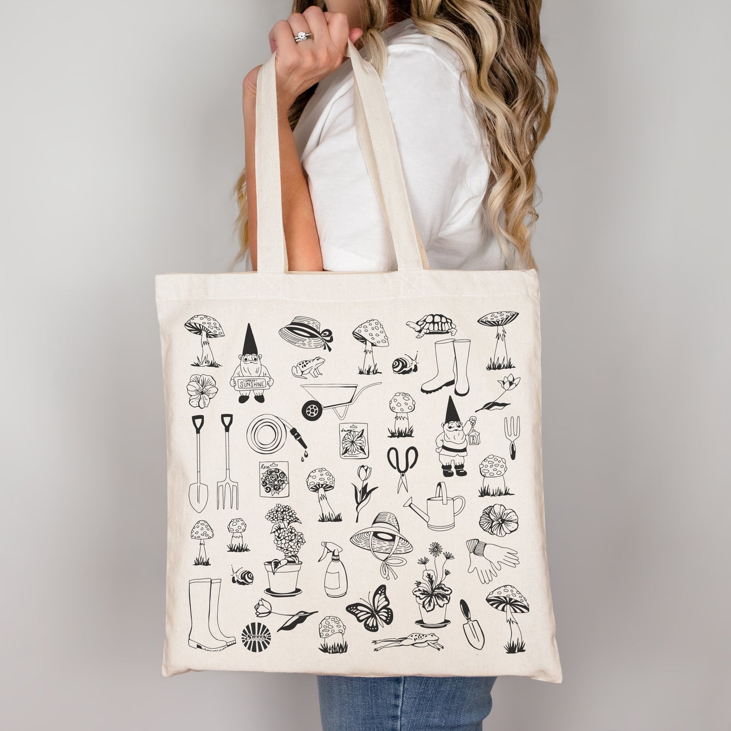 Person holding a tote bag with garden theme illustrations on a plain background