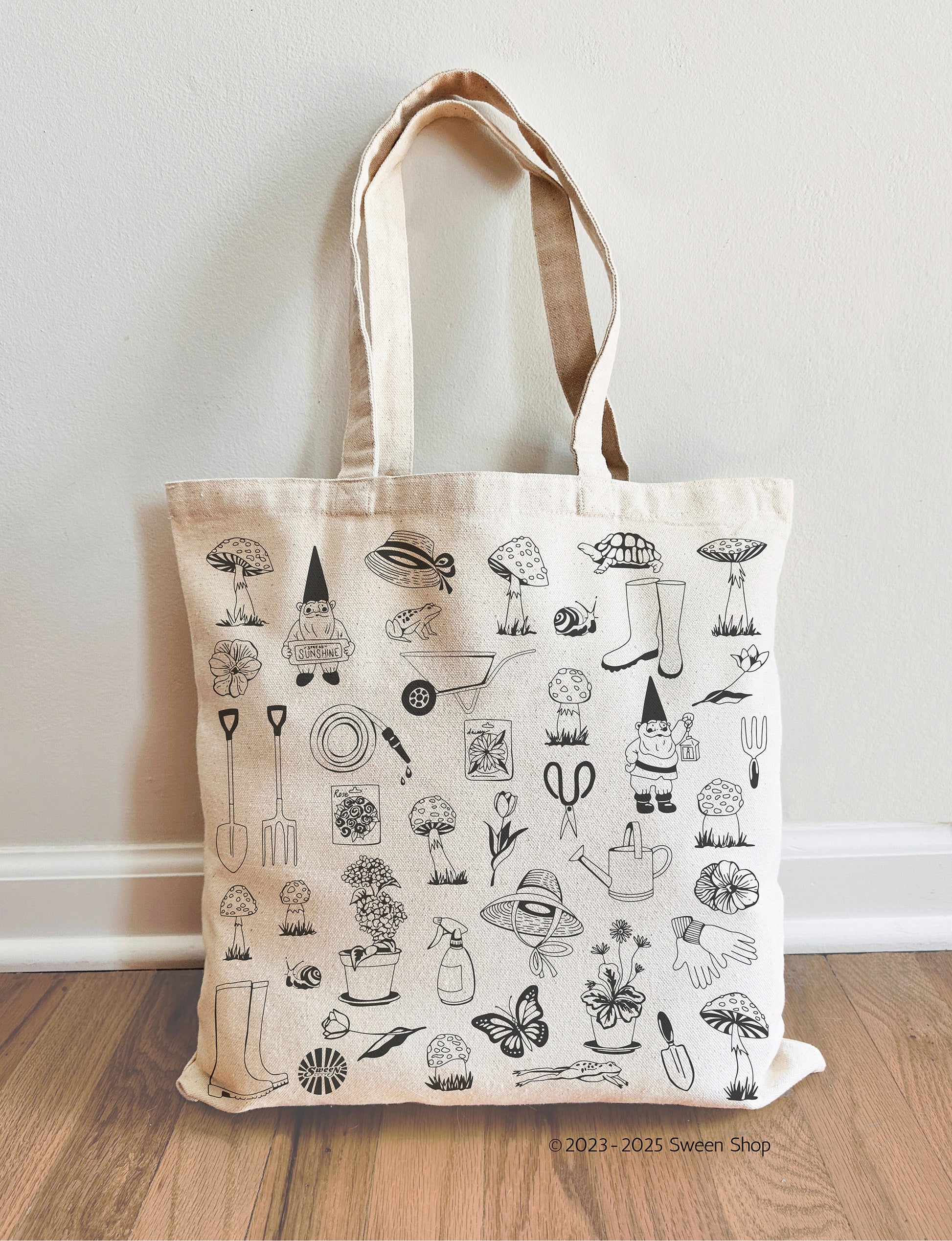 Tote bag with garden illustrations on a wooden floor against a white wall