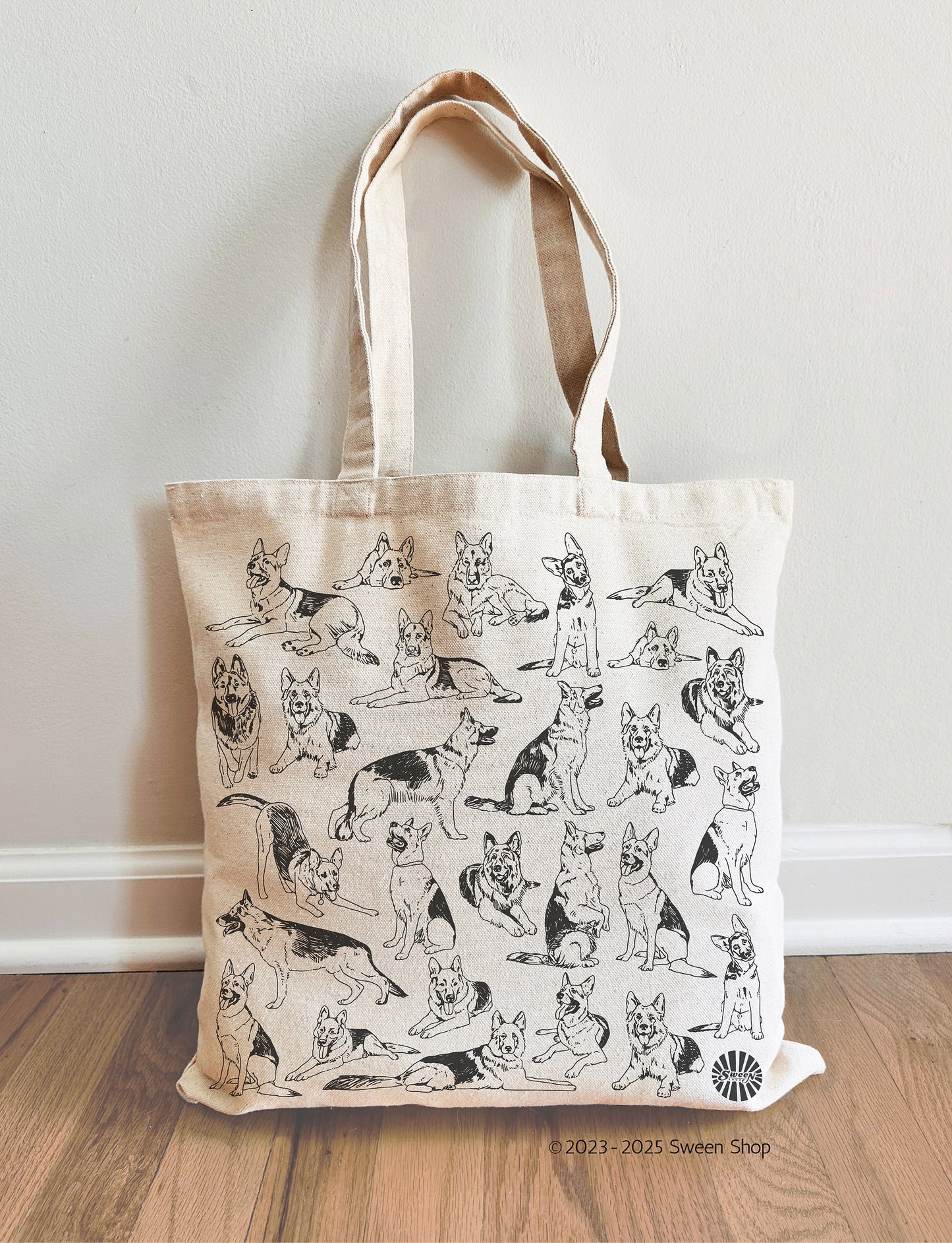 Tote bag with german shepherd pet dog illustrations on a wooden floor against a white wall.
