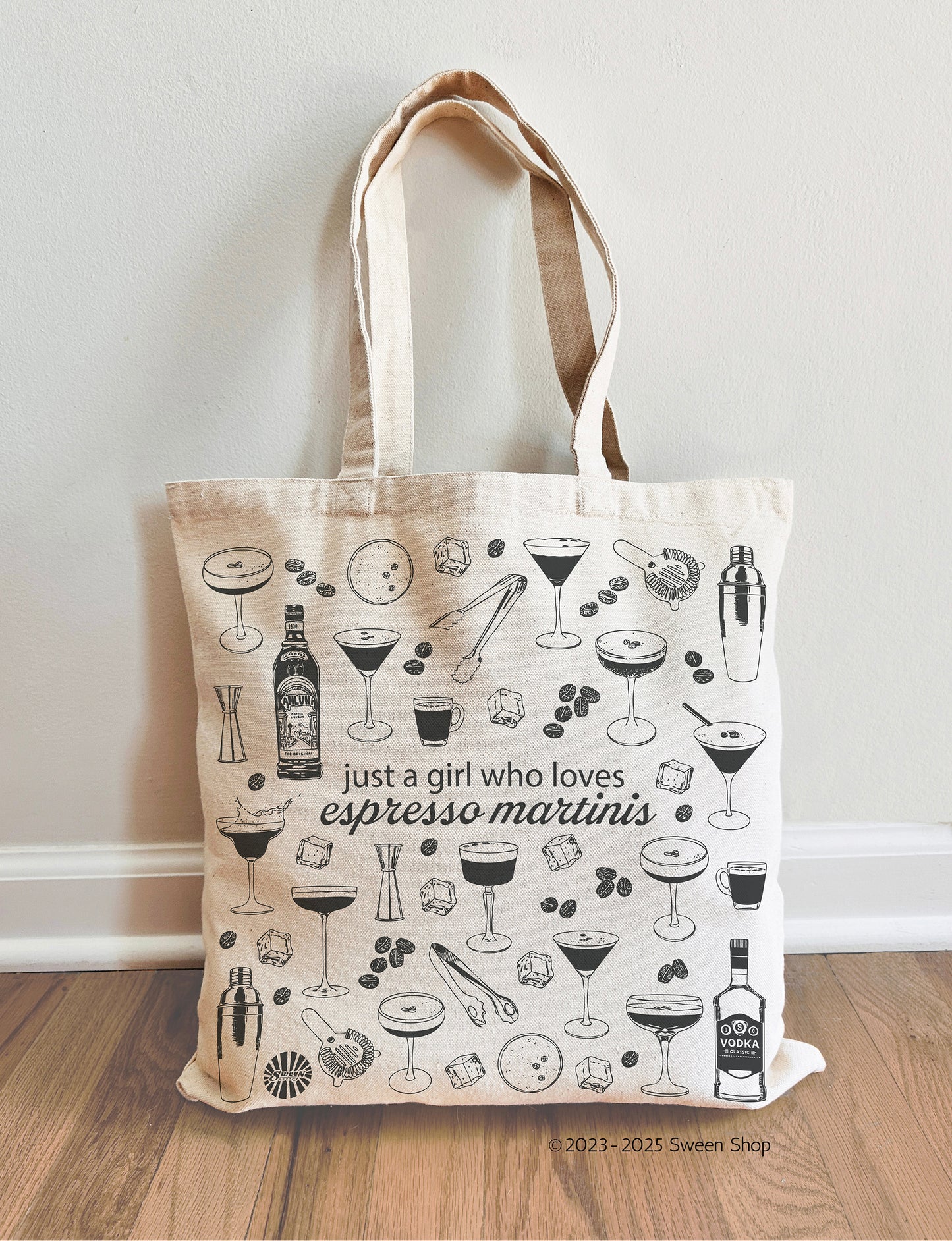 Tote bag with espresso martini cocktail illustrations and text on a wooden floor.