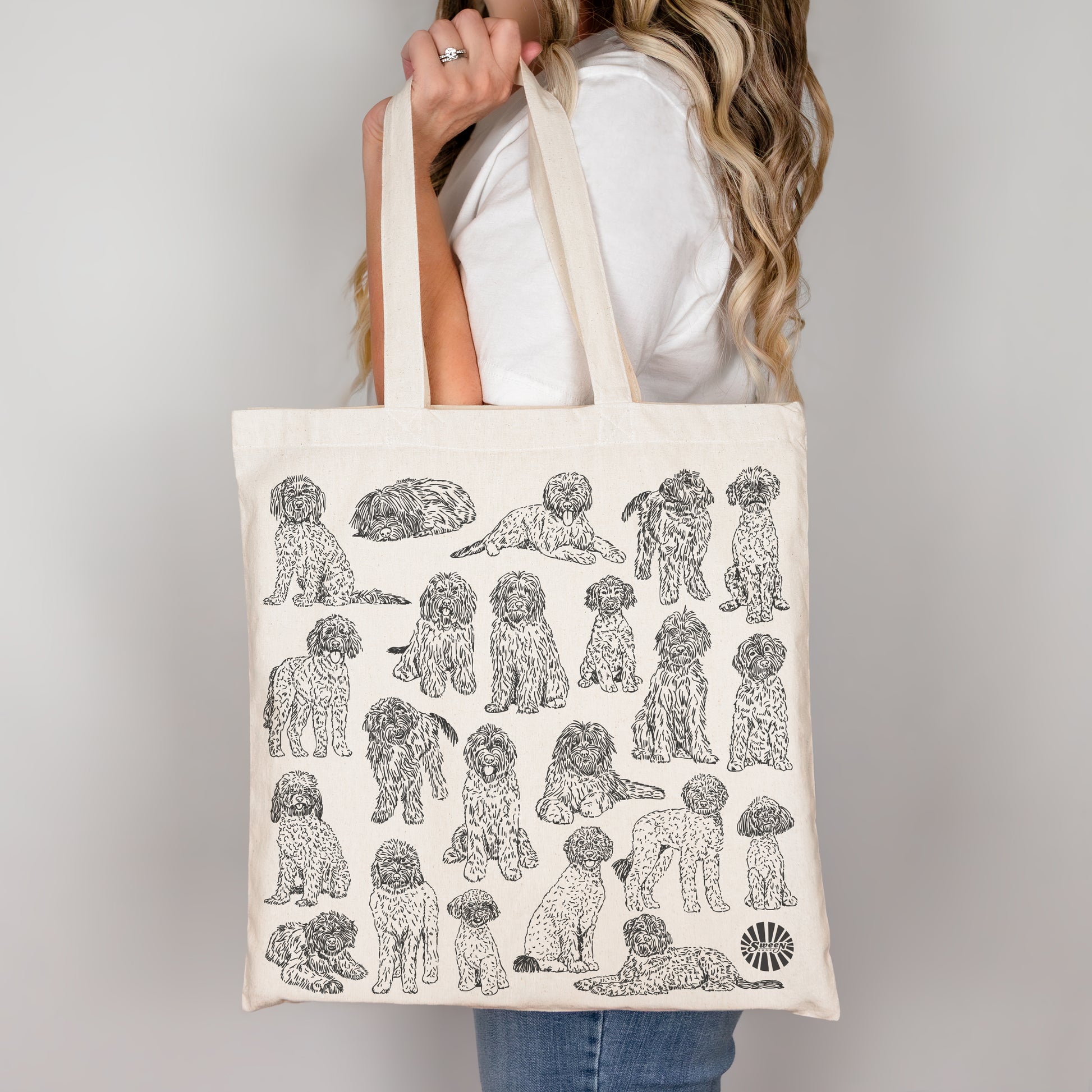 Tote bag with black and white pet golden doodle dog illustrations held by a person against a plain background