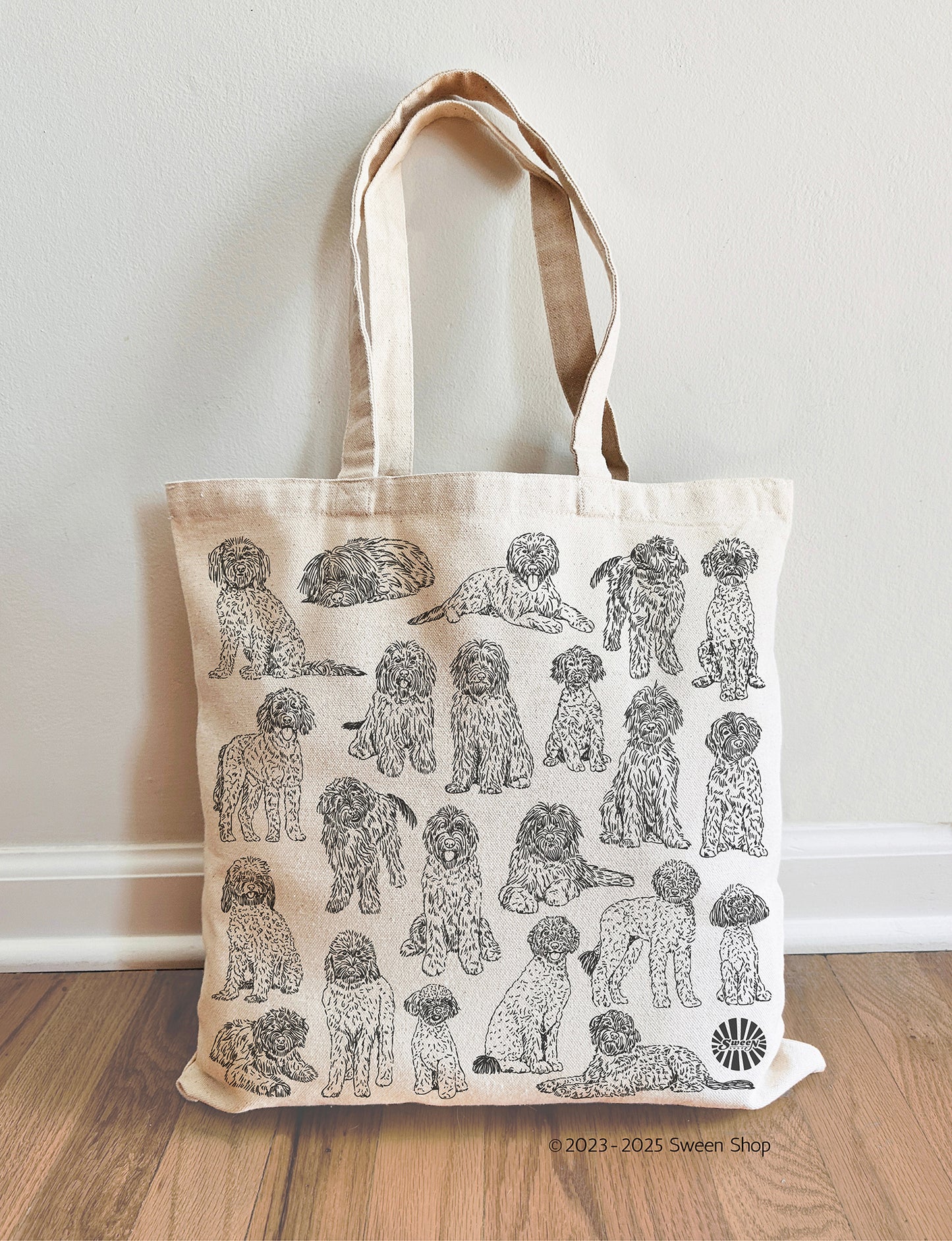 Tote bag with golden doodle pet dog illustrations on a wooden floor against a white wall
