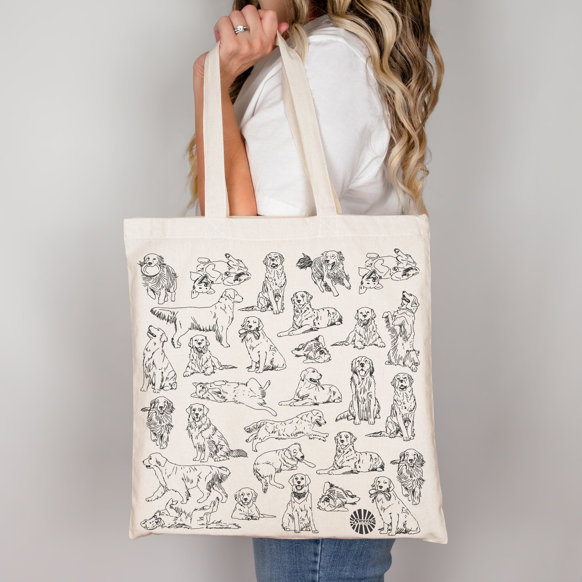 Tote bag with golden retriever pet dog illustrations held by a person against a plain background