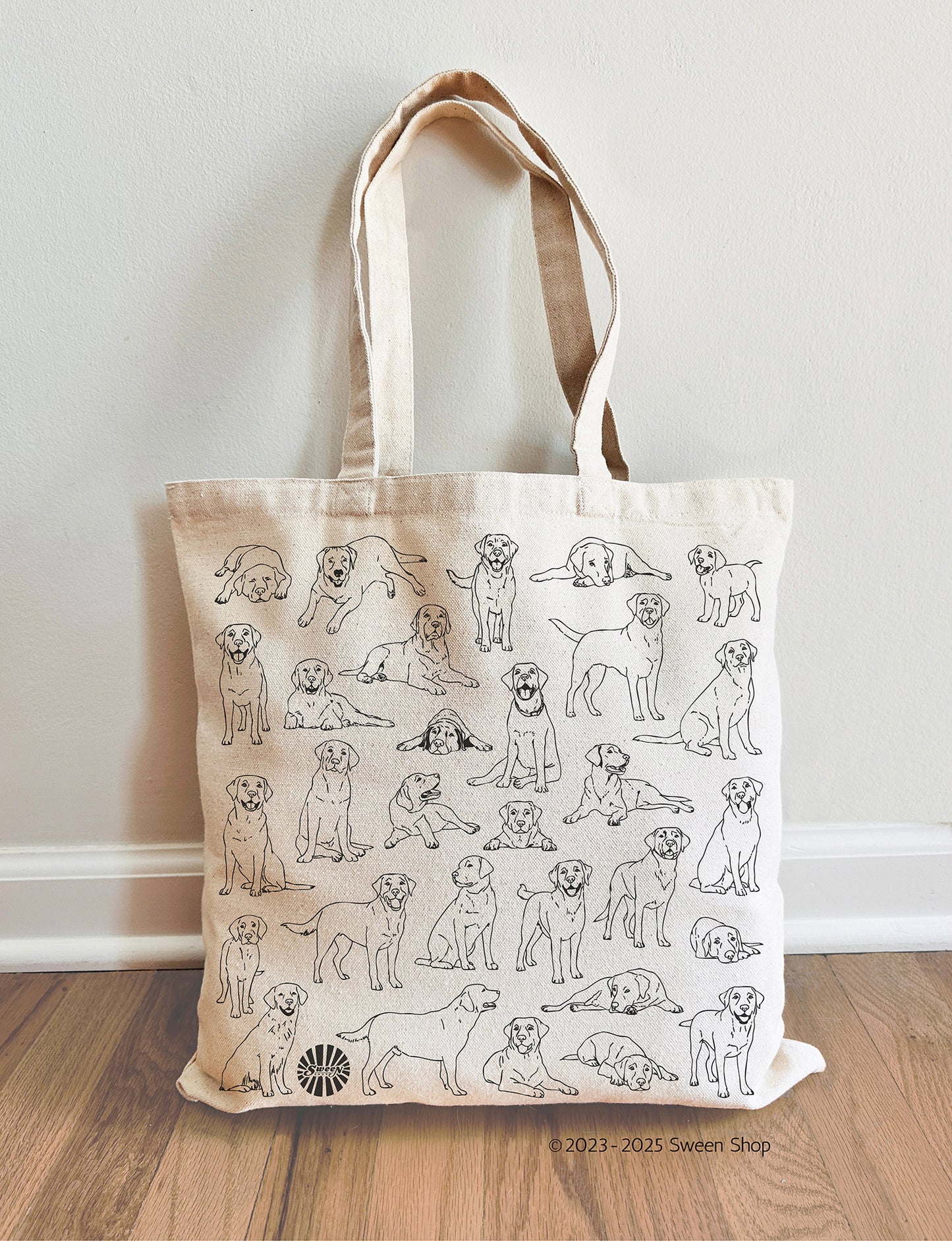 Tote bag with labrador pet dog illustrations on a wooden floor against a white wall