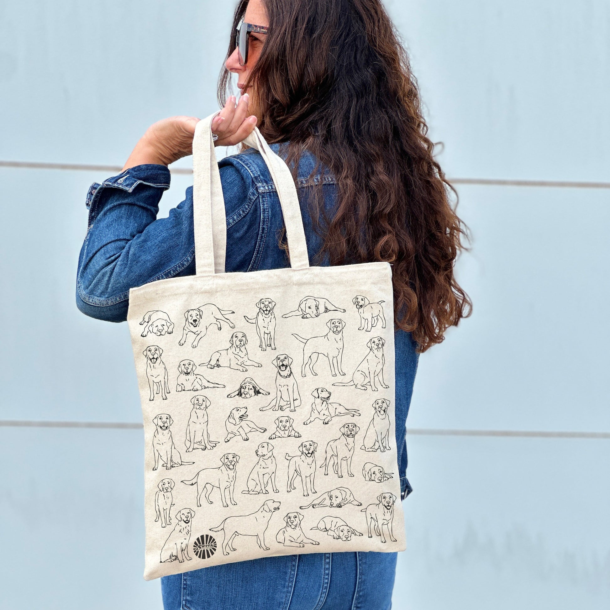 Person holding a tote bag with labrador pet dog illustrations against a light blue wall.