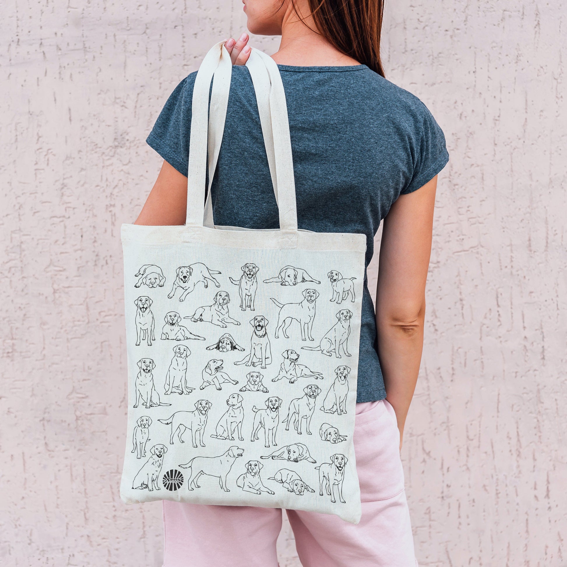 Person holding a tote bag with labrador pet dog illustrations against a light background