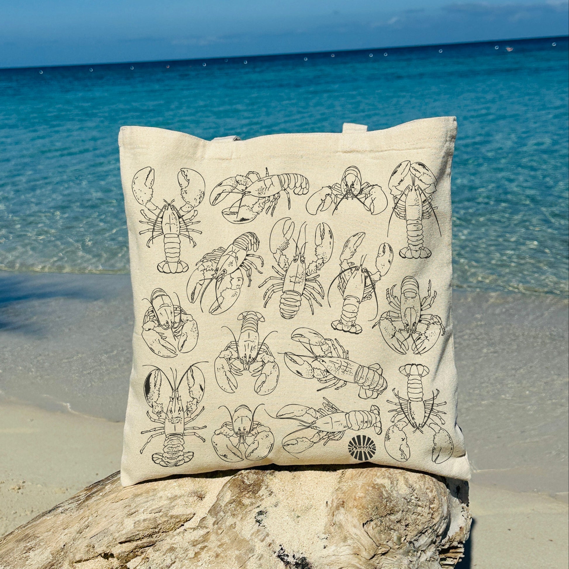 canvas tote bag with lobster design on a rock by the ocean