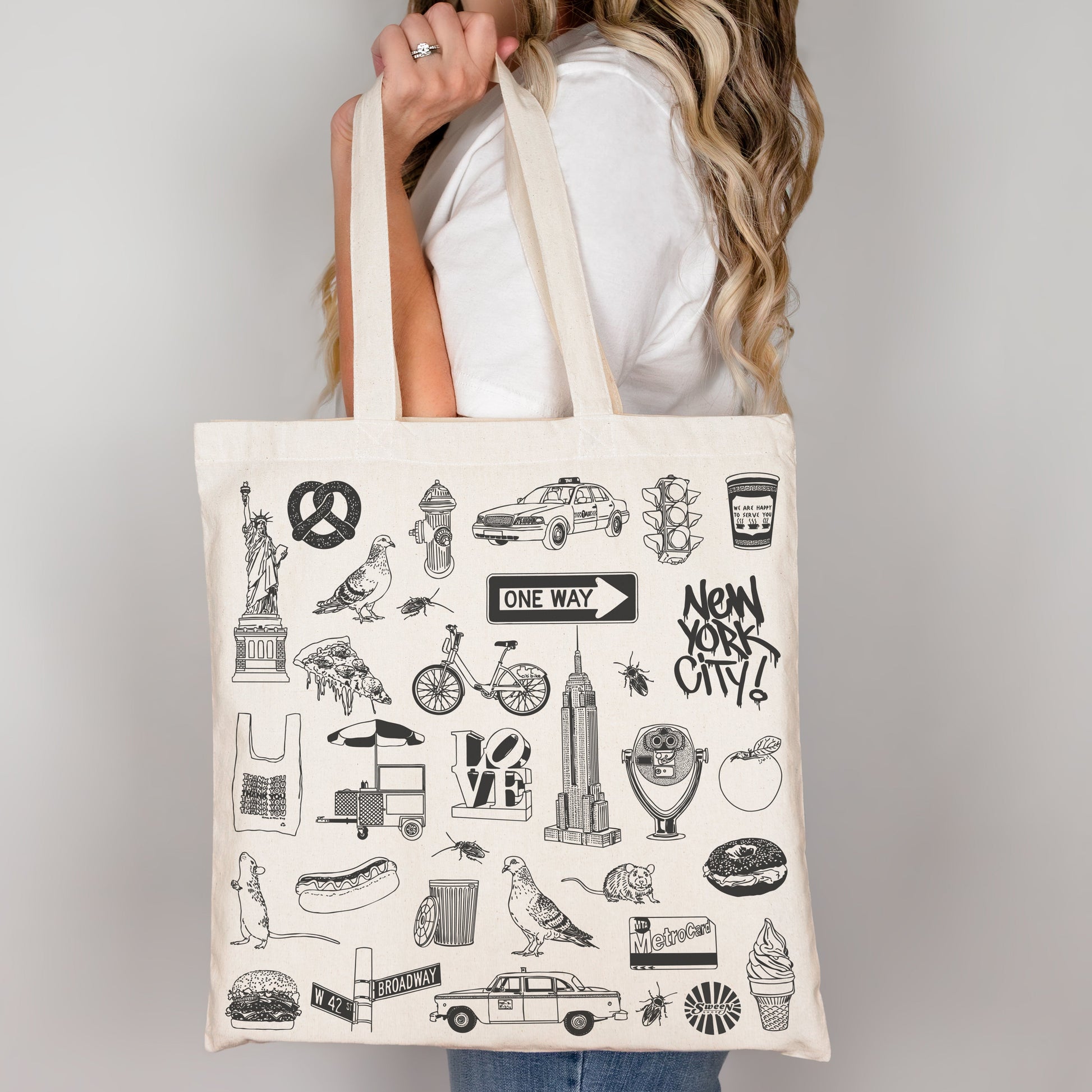 Tote bag with New York City-themed illustrations held by a person against a plain background