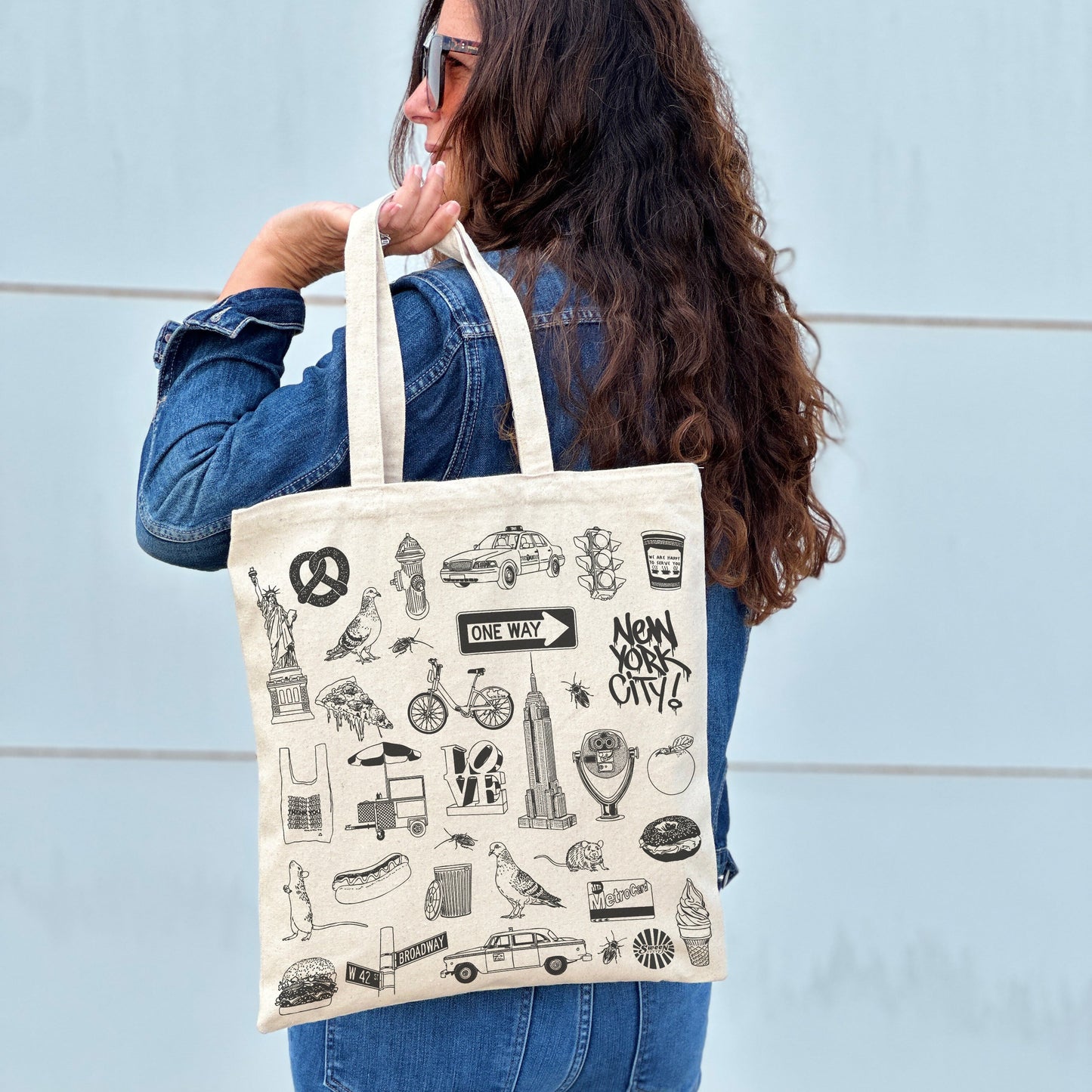 Person holding a tote bag with black New York city illustrations against a light blue wall.