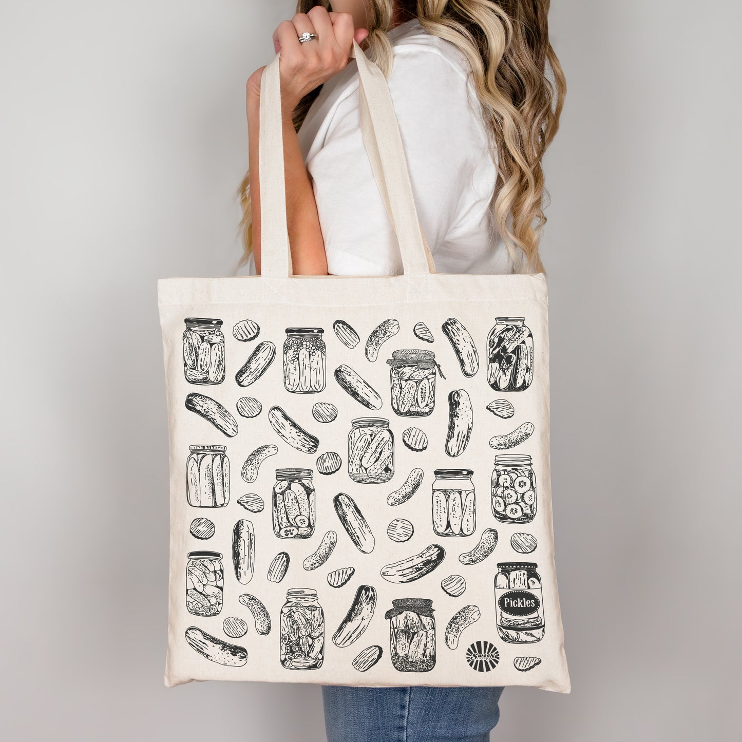 Person holding a tote bag with pickle and jar pattern against a plain background