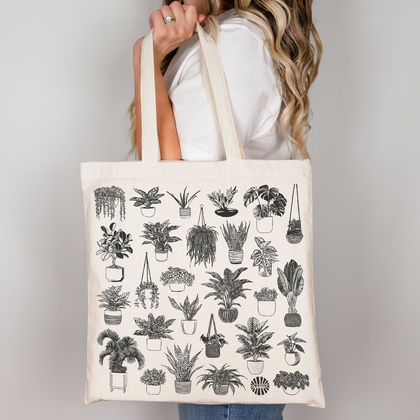 Person holding a tote bag with plant illustrations on a plain background