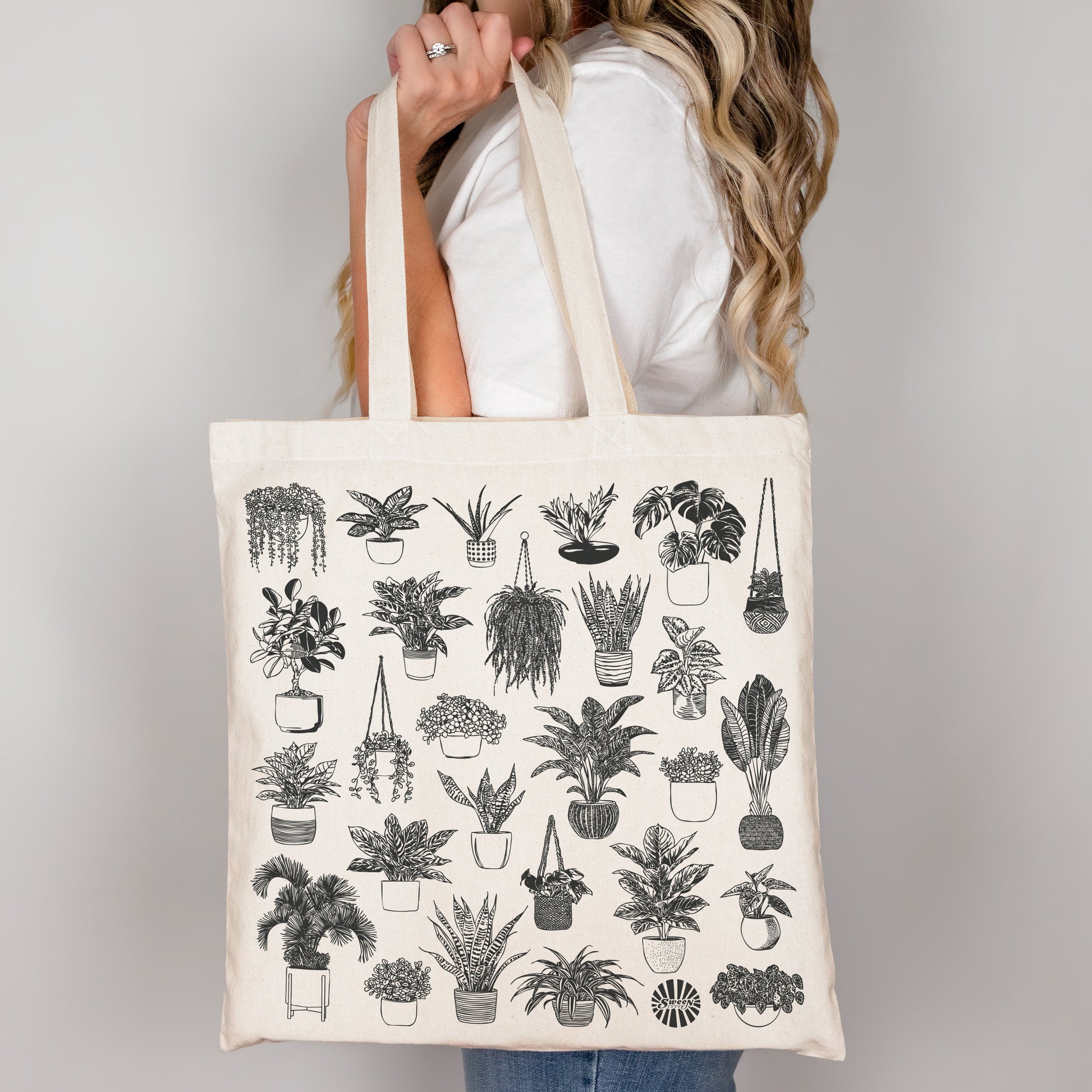 Person holding a tote bag with plant illustrations on a plain background