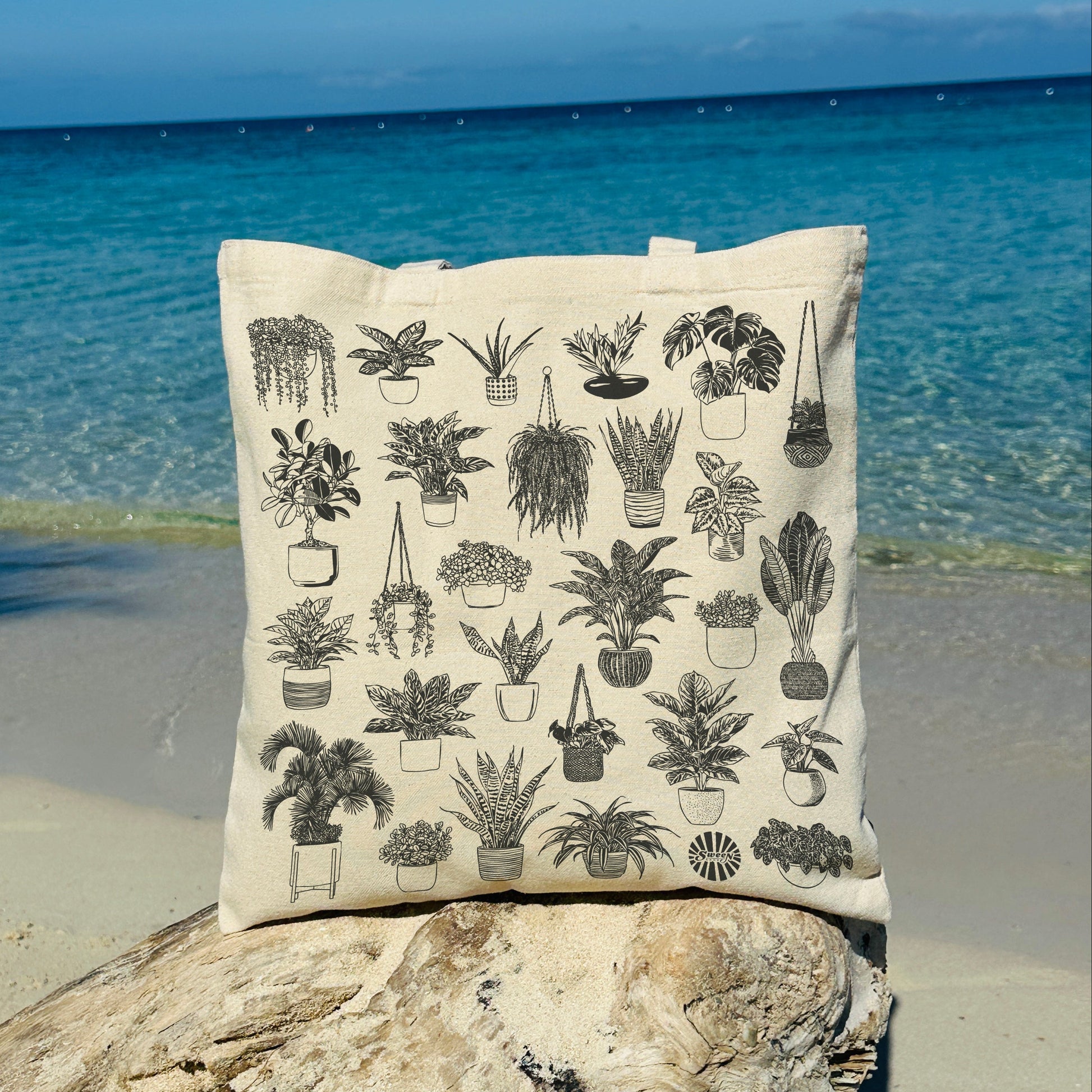 cotton canvas tote bag with plant illustrations on a rock by the ocean