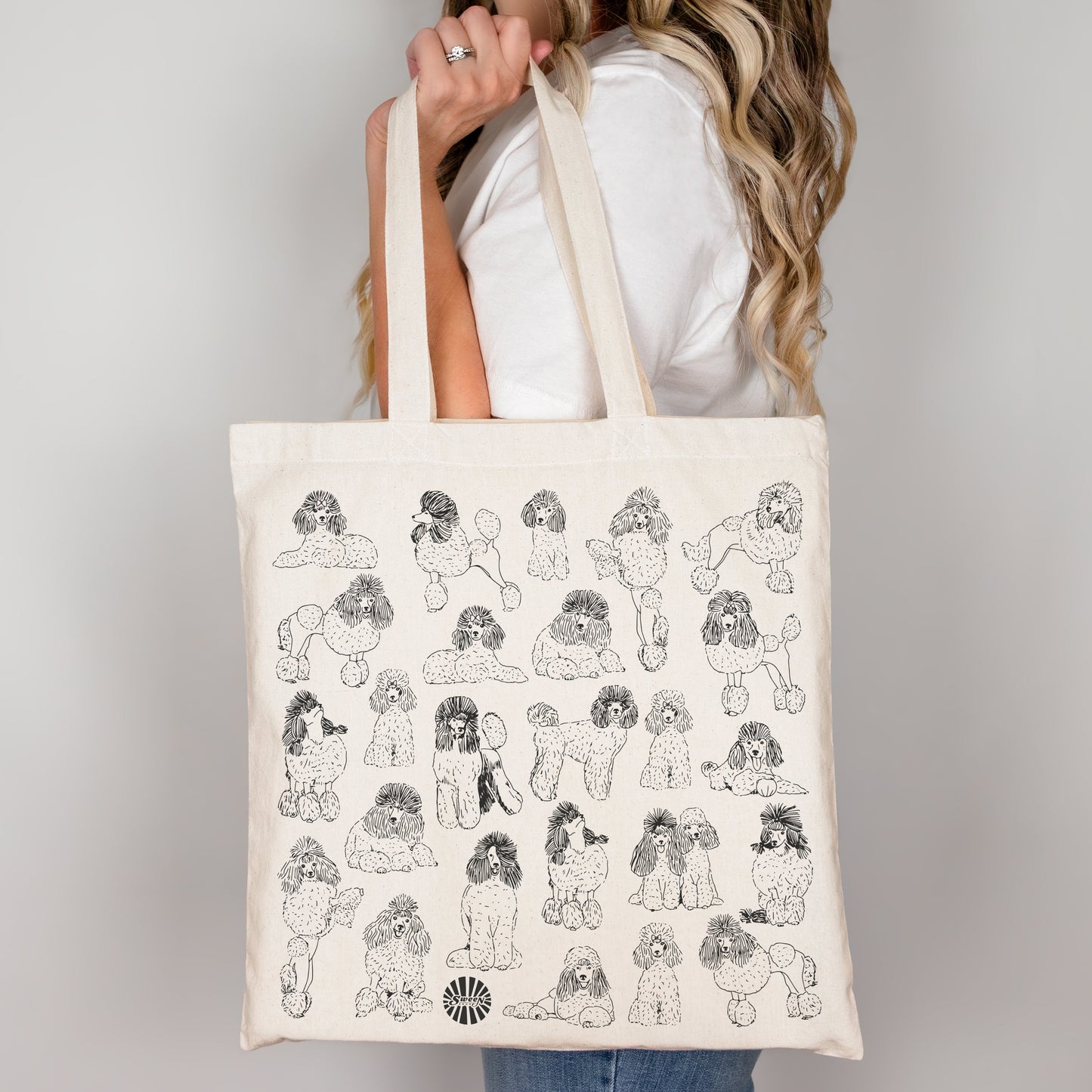 Person holding a tote bag with black poodle dog illustrations on a plain background