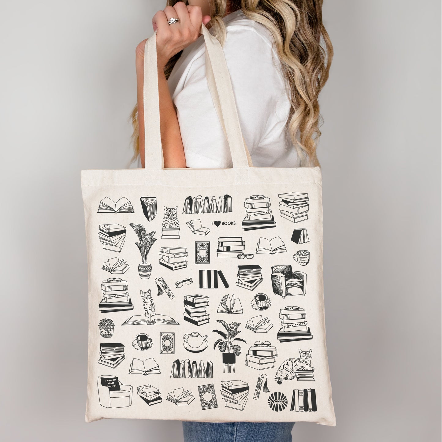 Person holding a tote bag with black line drawing illustrations of reading books plants coffee and cats on a plain background