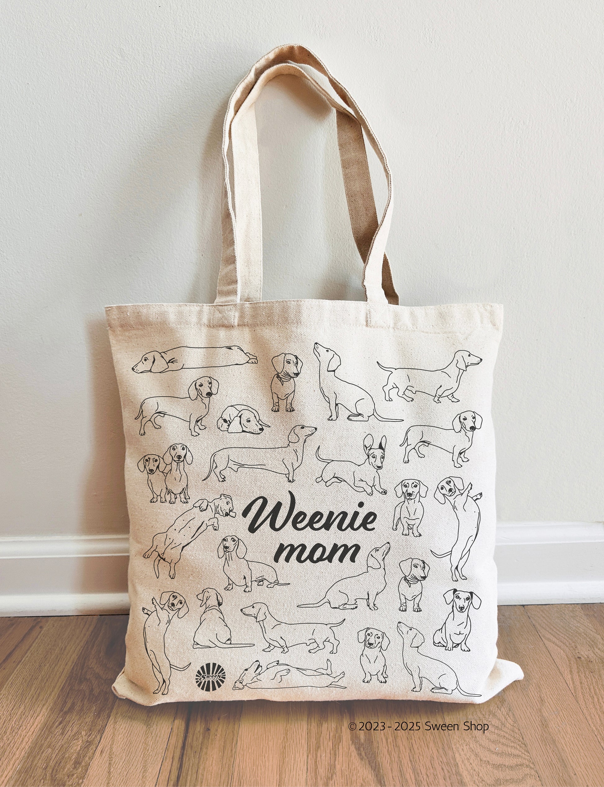 Tote bag with illustrations of Dachshund dogs and 'Weenie mom' text on a wooden floor.